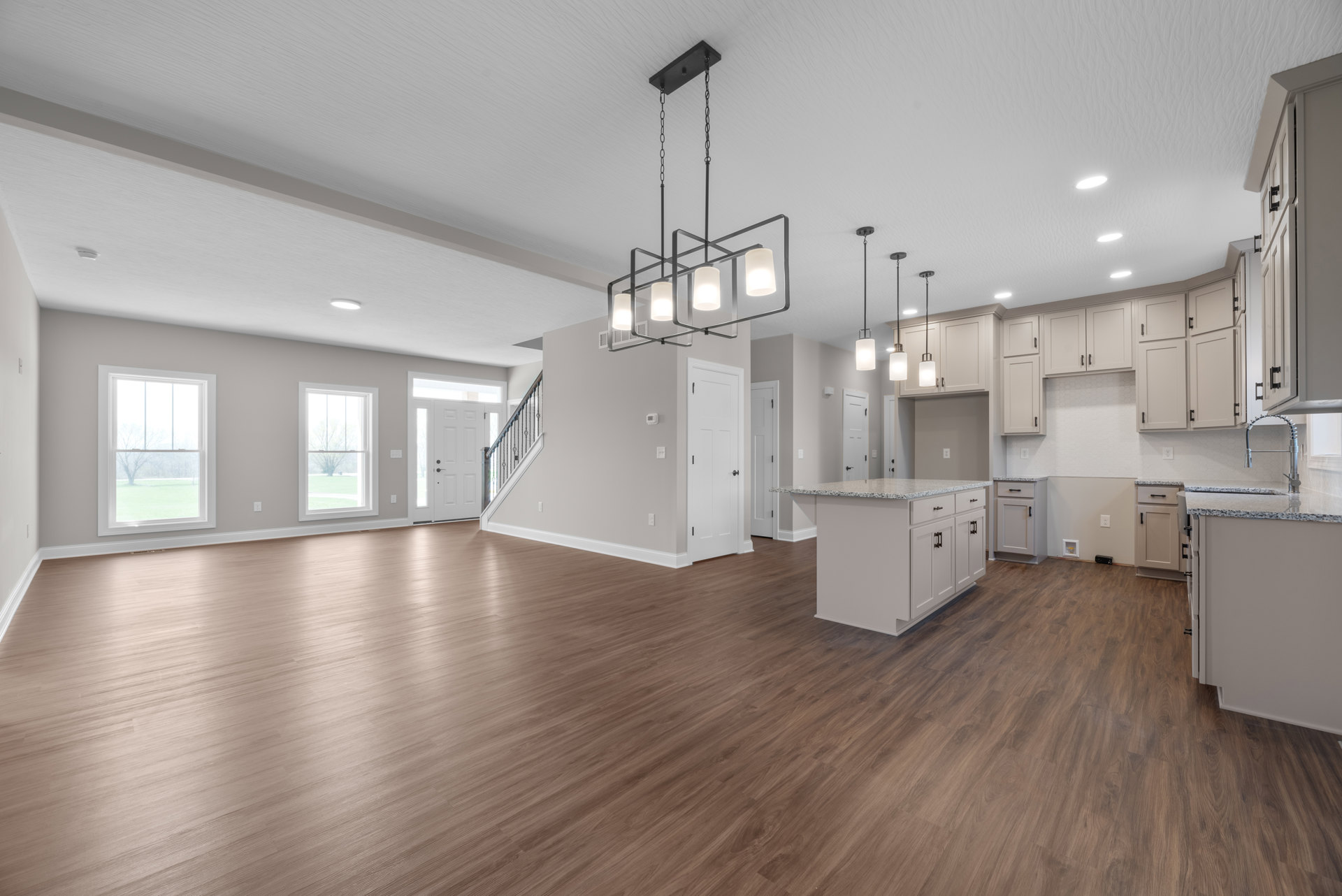 Spacious open floor plan featuring hardwood flooring, white kitchen island with marble countertop, white cabinetry, large windows overlooking lawn and trees, white walls, and a