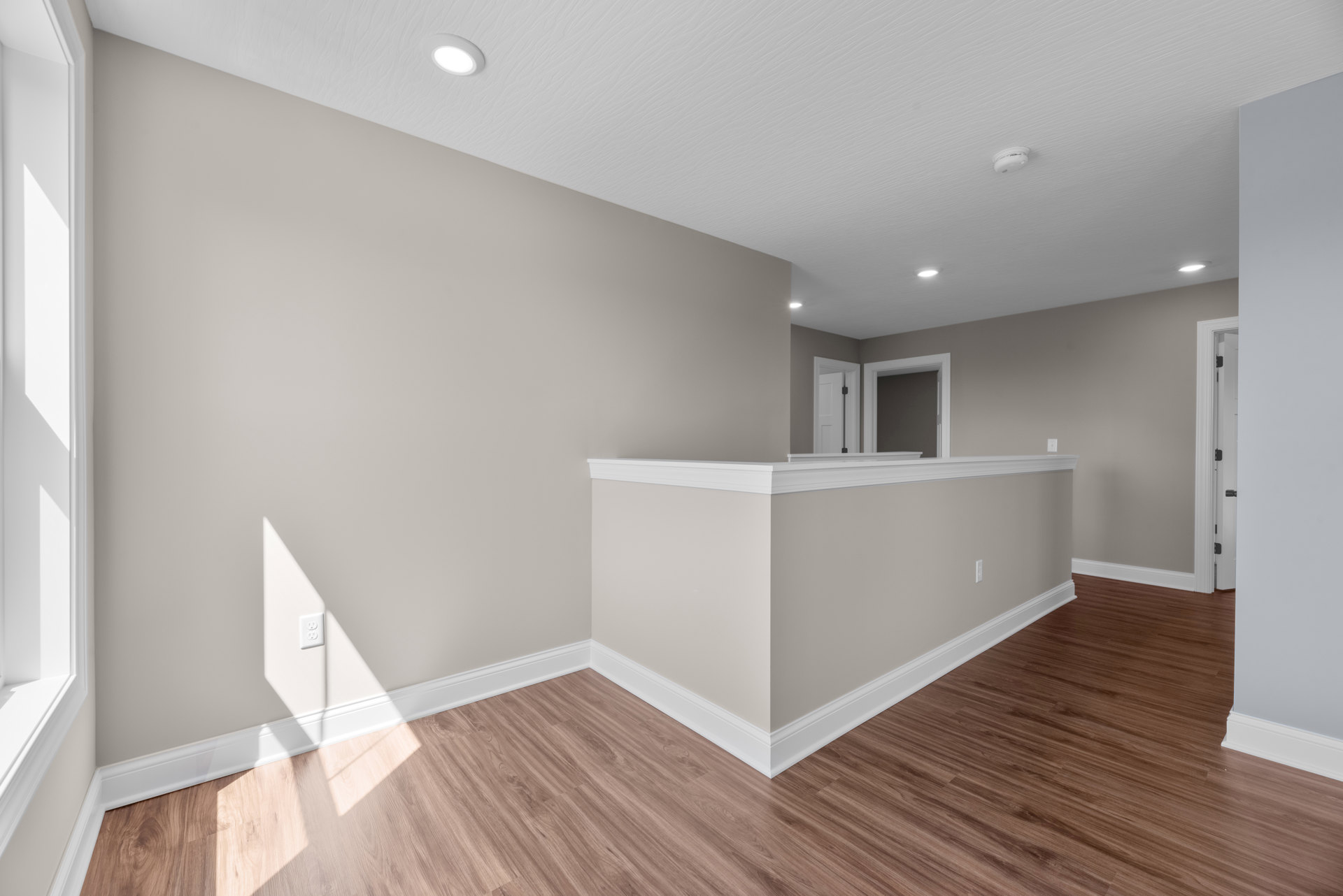 Corner of a room with hardwood flooring, white plaster walls, and a close-up view of a door frame and hinge