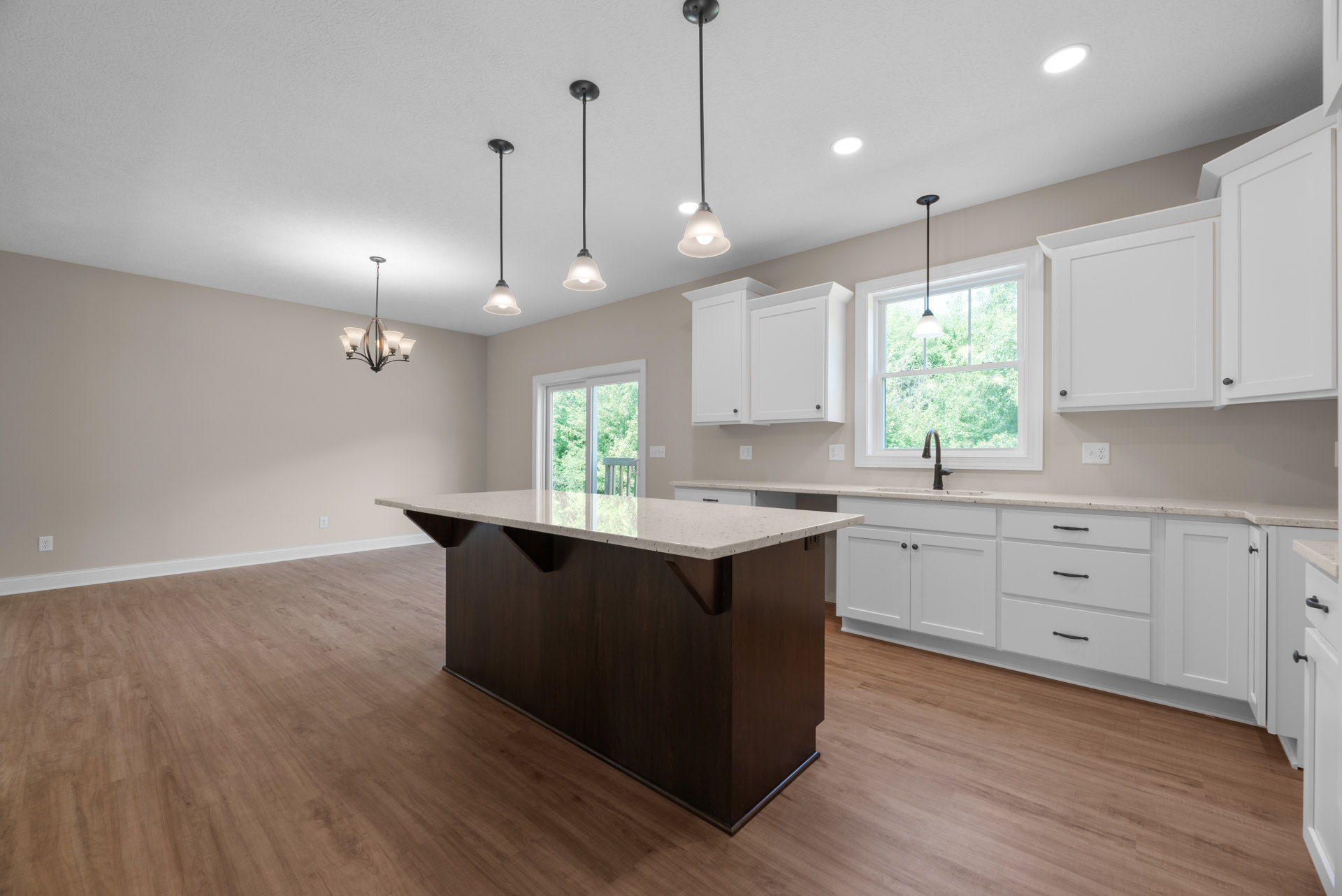 Modern kitchen featuring a central island with light-colored countertop, white cabinetry, stainless steel sink beneath a window, pendant light fixtures, and black metal support