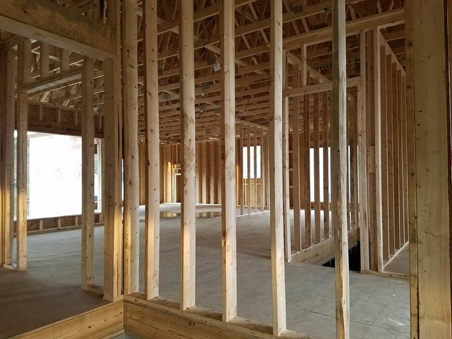 Exposed wood framing and beams in an unfinished room with a window, white insulation panels, and visible roof trusses