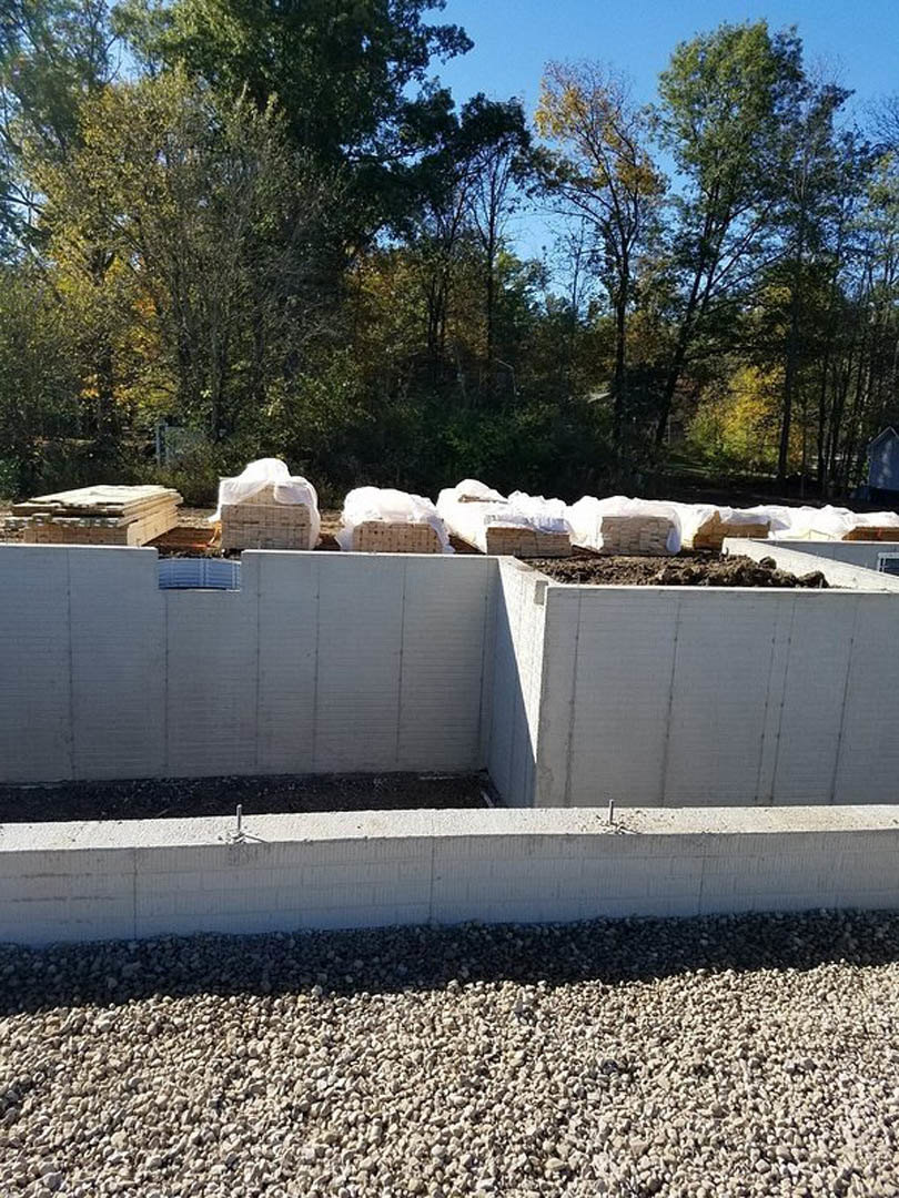 Construction site with white concrete wall, stacked pallets, pile of dirt, scattered white rocks, and trees in the background