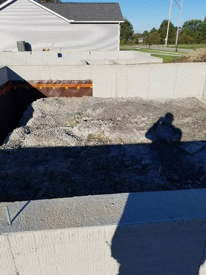 Shadow of a person cast on a pile of dirt at a construction site, with white brick wall and metal fence visible in the background