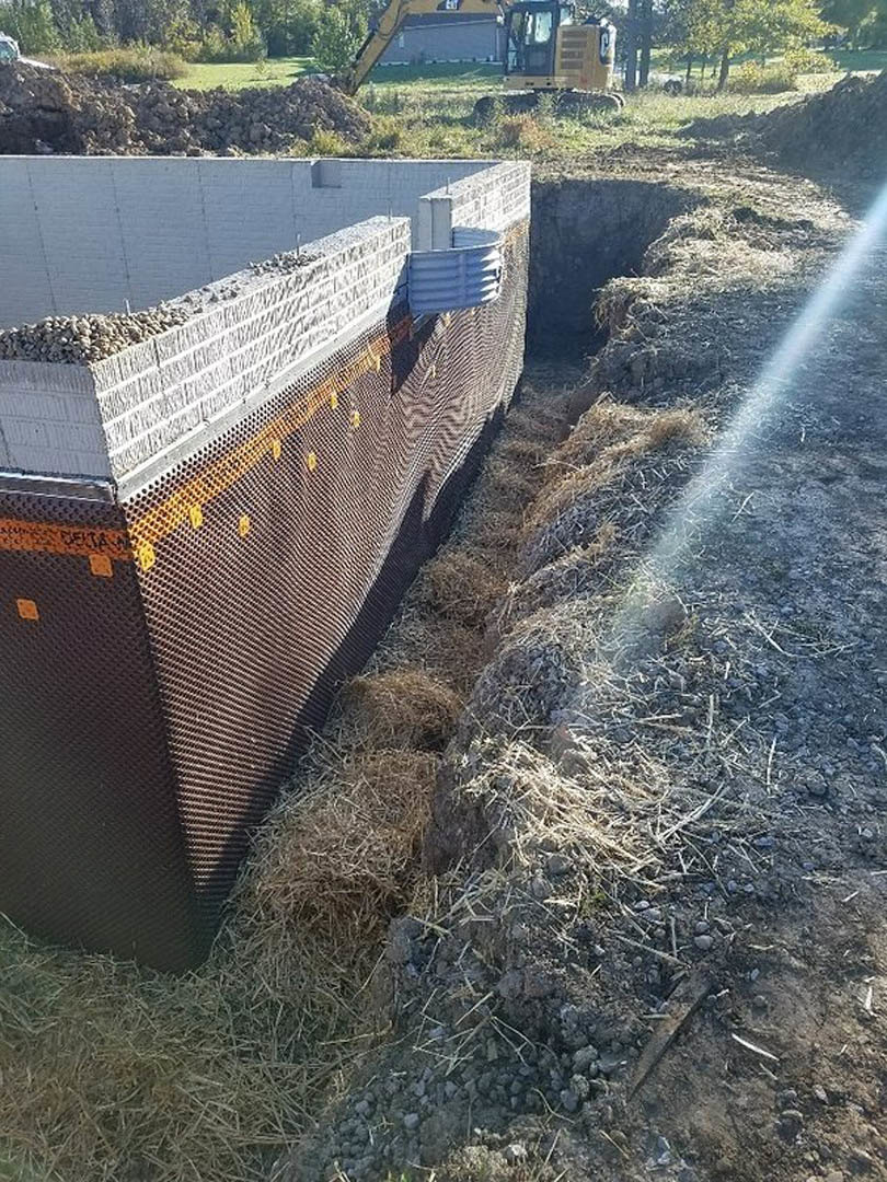Excavated dirt pit bordered by a stone retaining wall, grassy lawn, and construction equipment