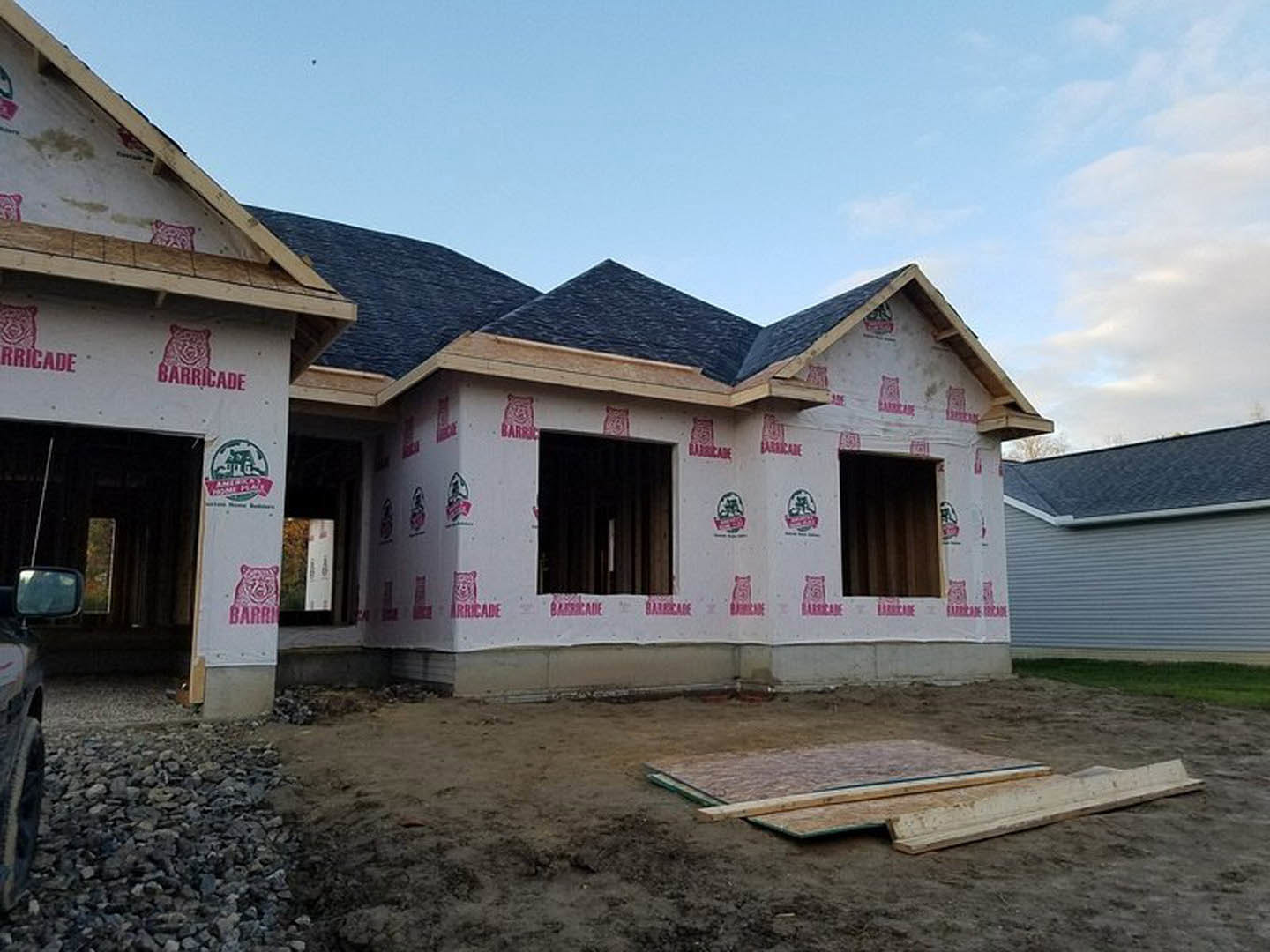 Partially built house with exposed plywood sheathing, red inspection stickers on exterior walls, unfinished windows, and roof under cloudy sky
