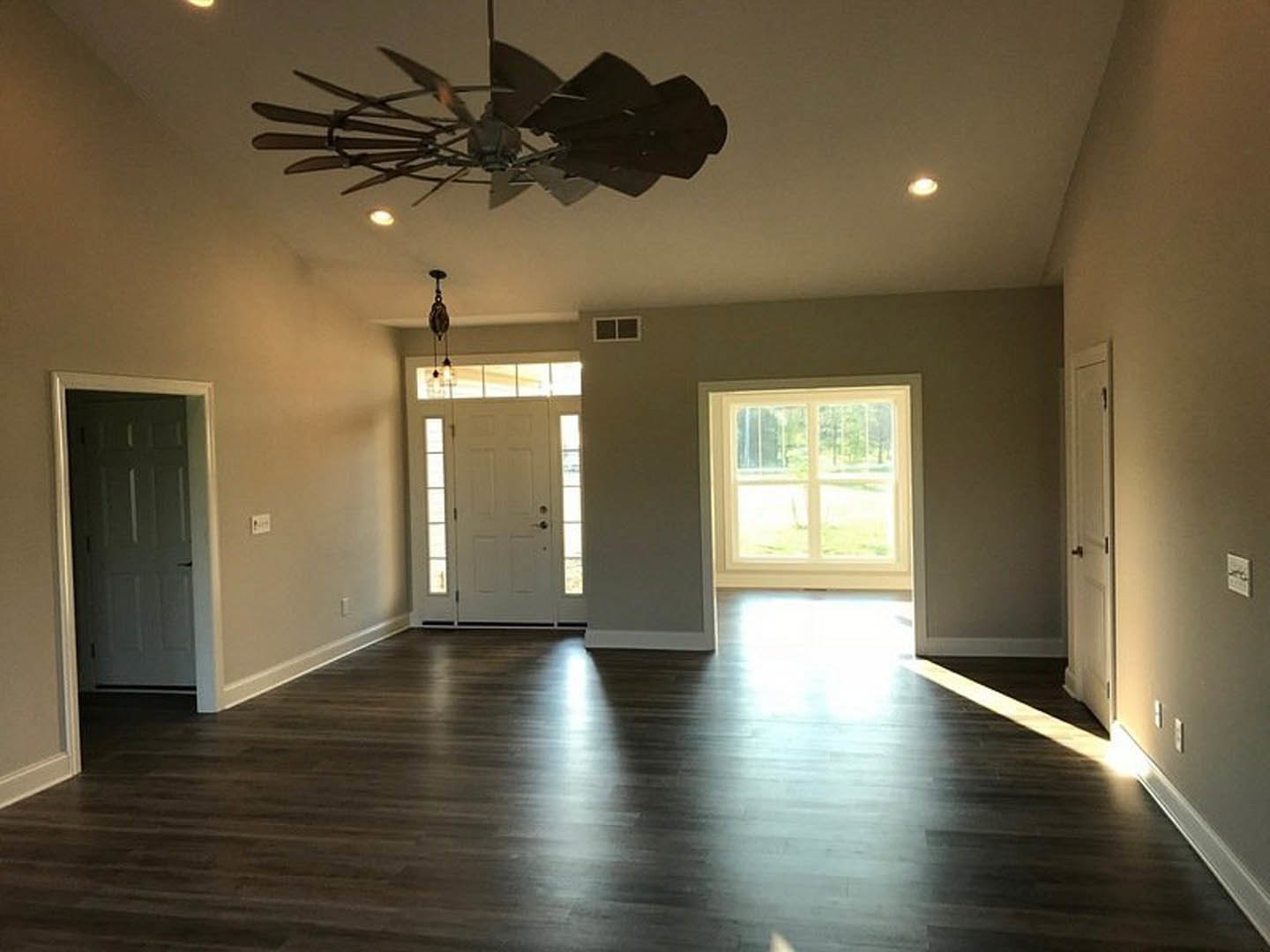 Spacious room with laminate flooring, white walls, ceiling fan, and two white doors, one featuring a window with outdoor view