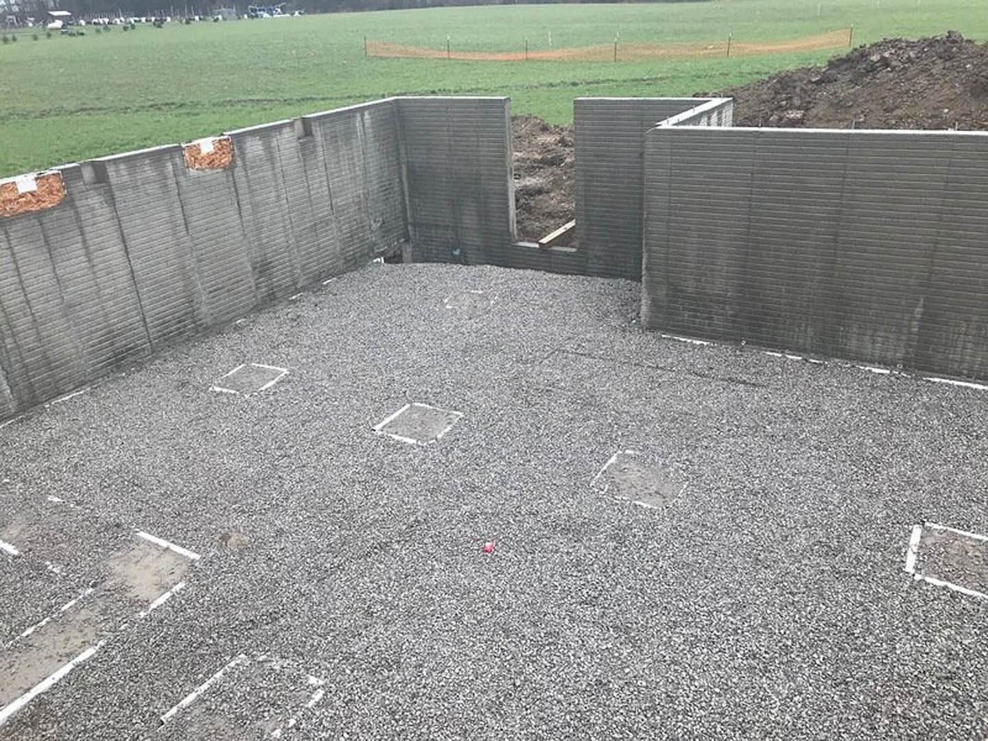 Concrete foundation wall with a rectangular opening, gravel floor, grey brick wall, grassy hill in background