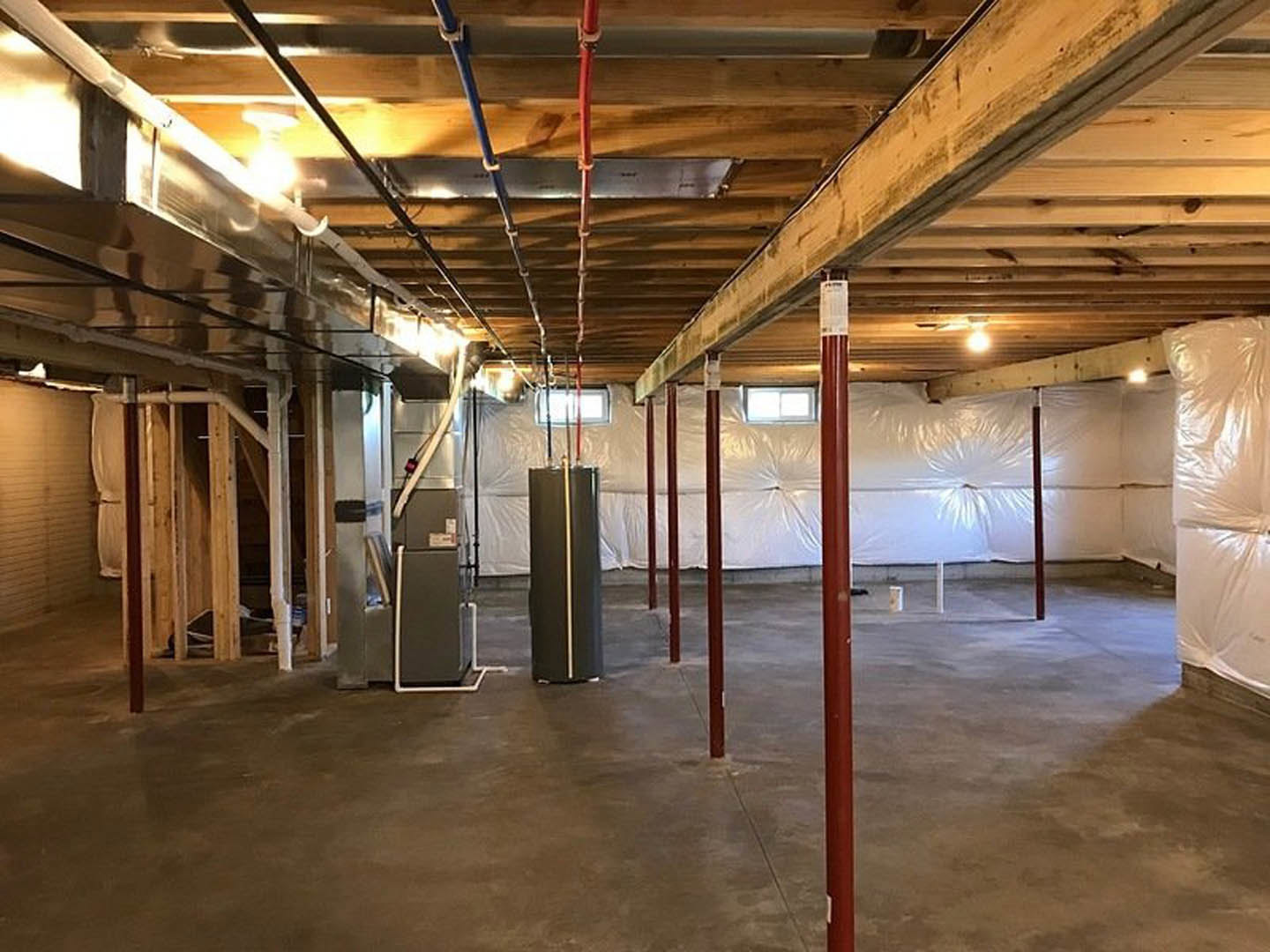 Basement room with exposed steel pipes, white refrigerator, concrete floor, and white plastic wall covering