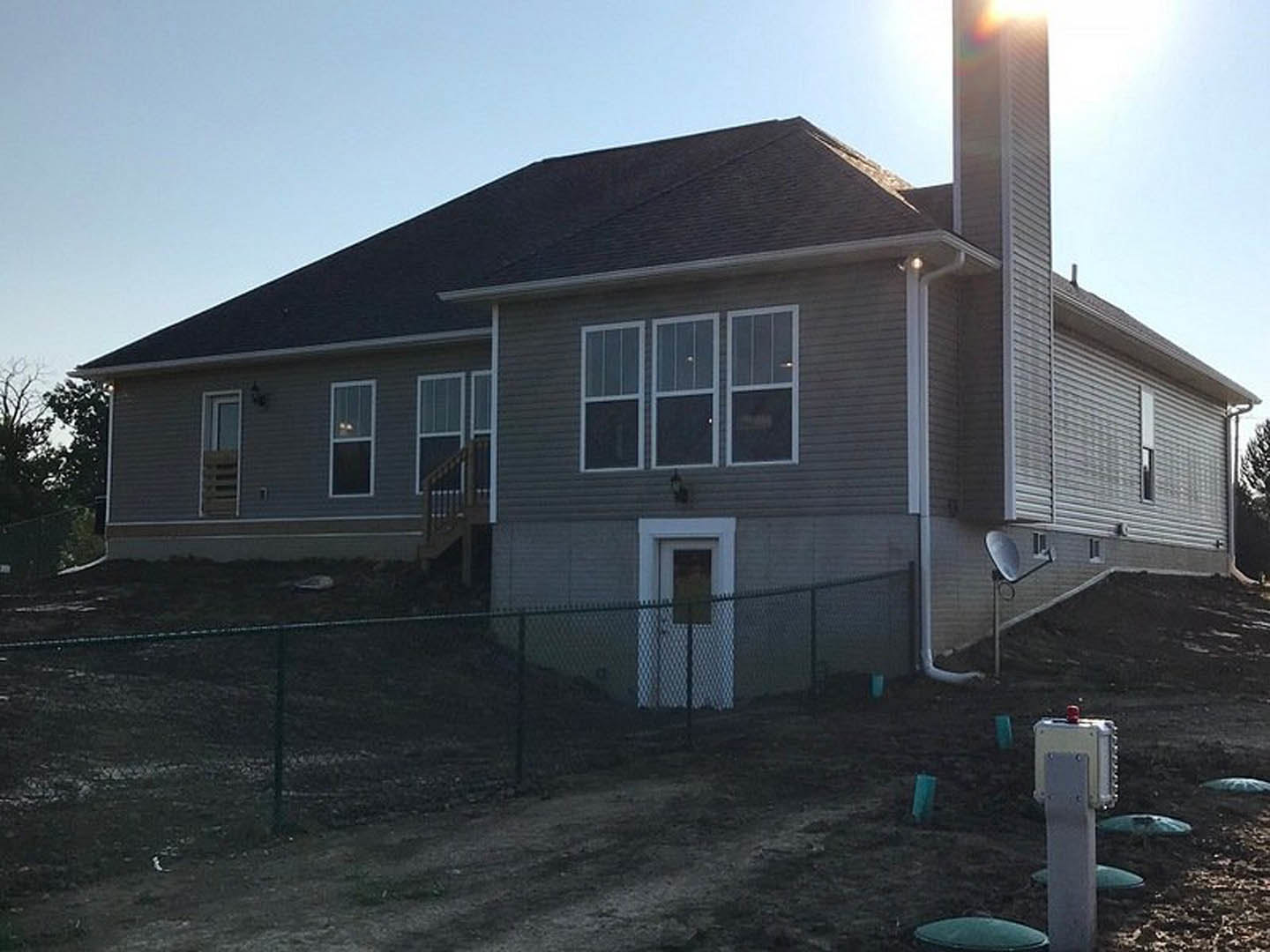Two-story cottage with light siding, gabled roof, white-trimmed windows, and wooden fence enclosing a grassy yard with mature trees