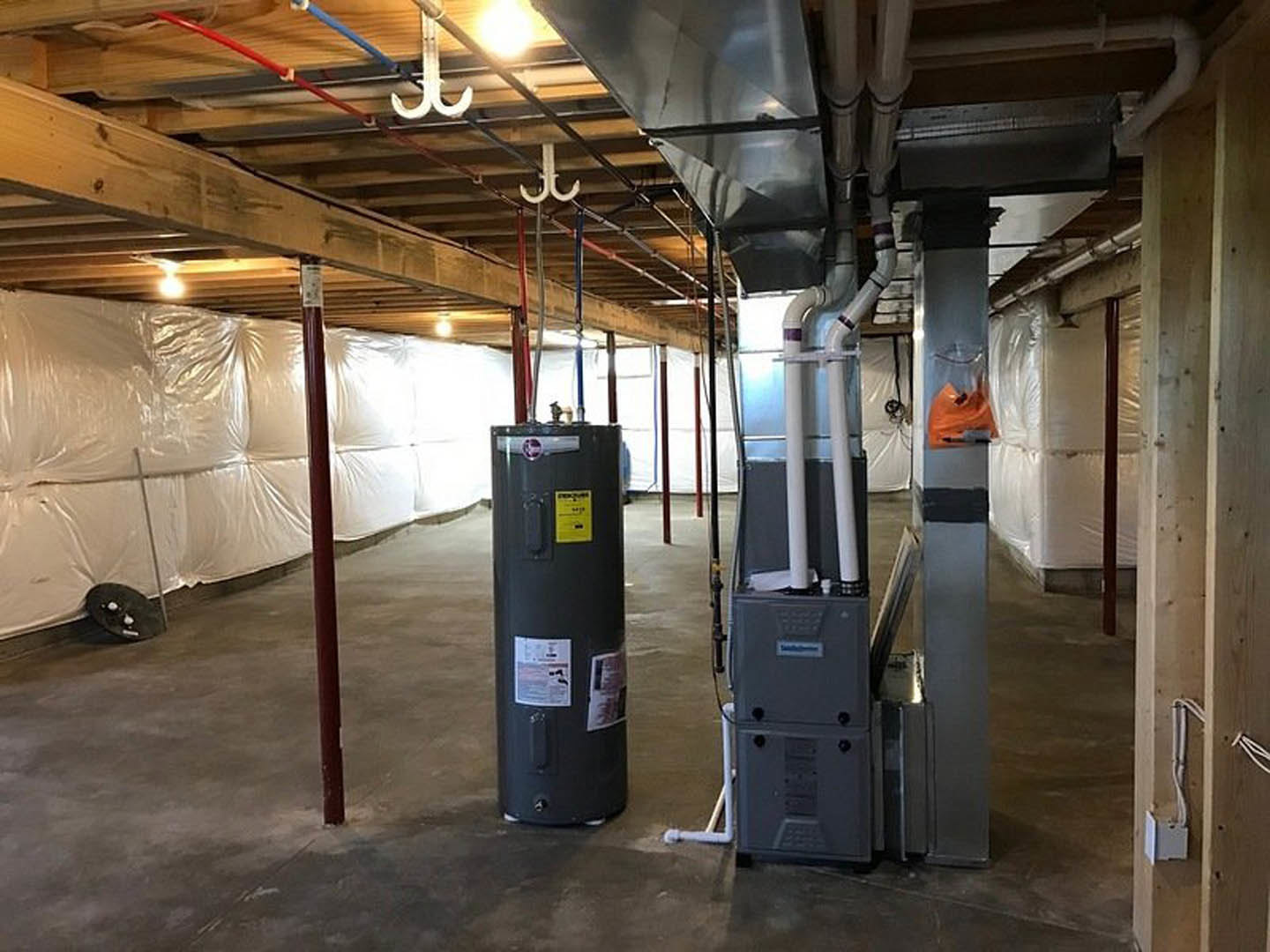 Spacious basement with exposed steel ceiling, large black boiler featuring yellow safety label, white plastic wall covering, yellow caution sign, and machine with white tubes.