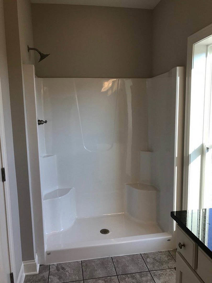 White tile shower with glass door, black vanity countertop, chrome shower head, grey tile walls, and window providing natural light