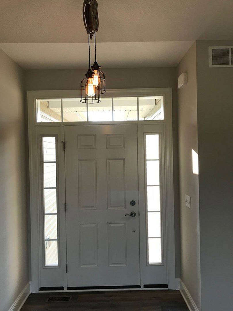 White paneled door with glass windows, black ceiling light fixture, white walls with crown molding, wall vent, and smooth black surface in foreground
