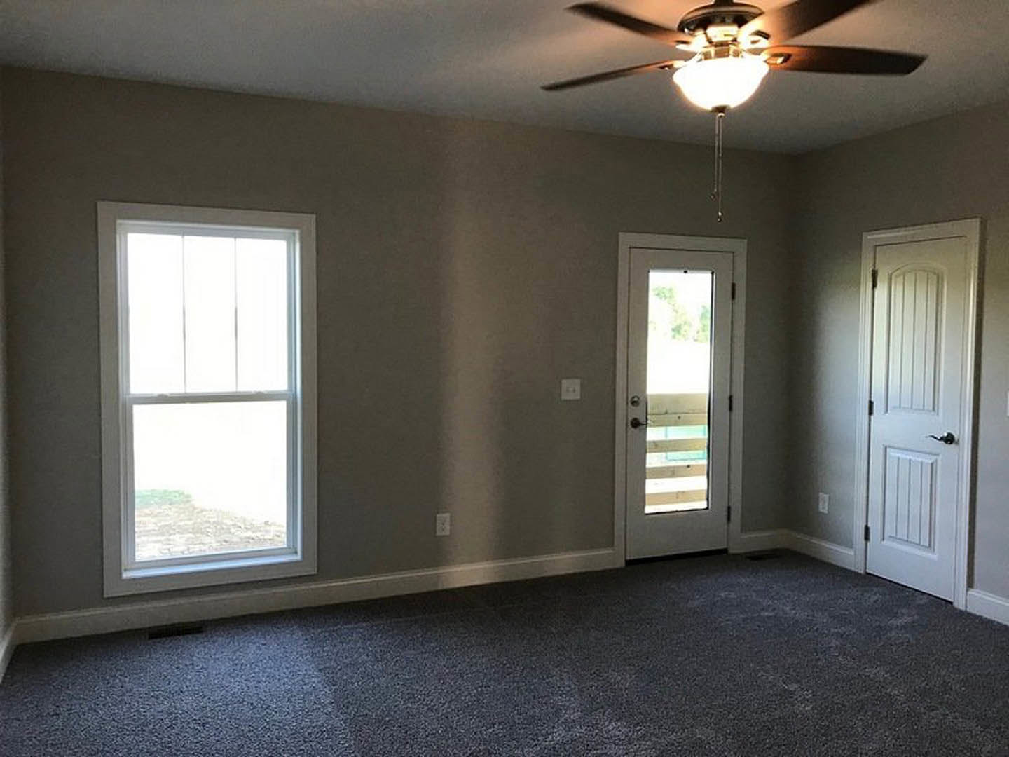 Carpeted room with a ceiling fan and light, white framed window, two white doors—one with glass panels and one with a black handle.