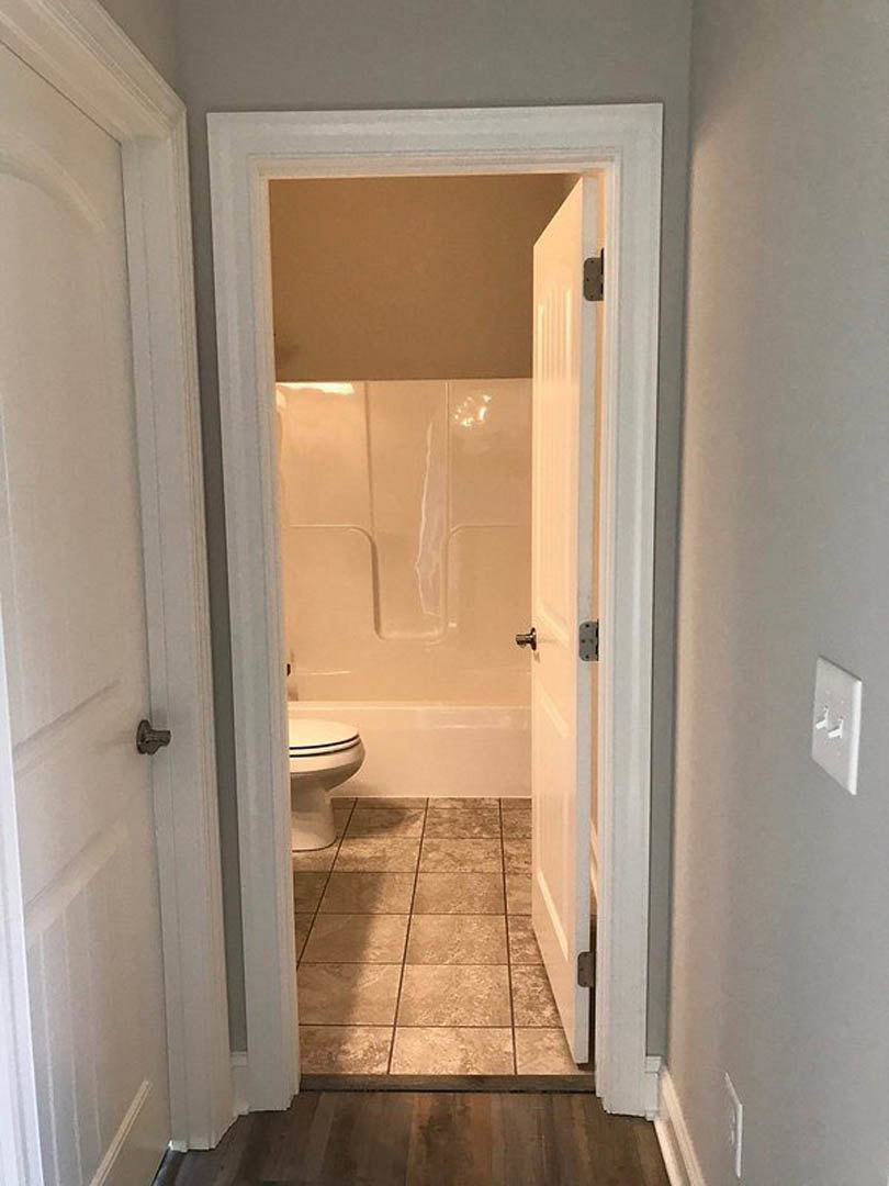 Bathroom with white toilet, gray tile floor, white door, and visible electrical outlet on plaster wall