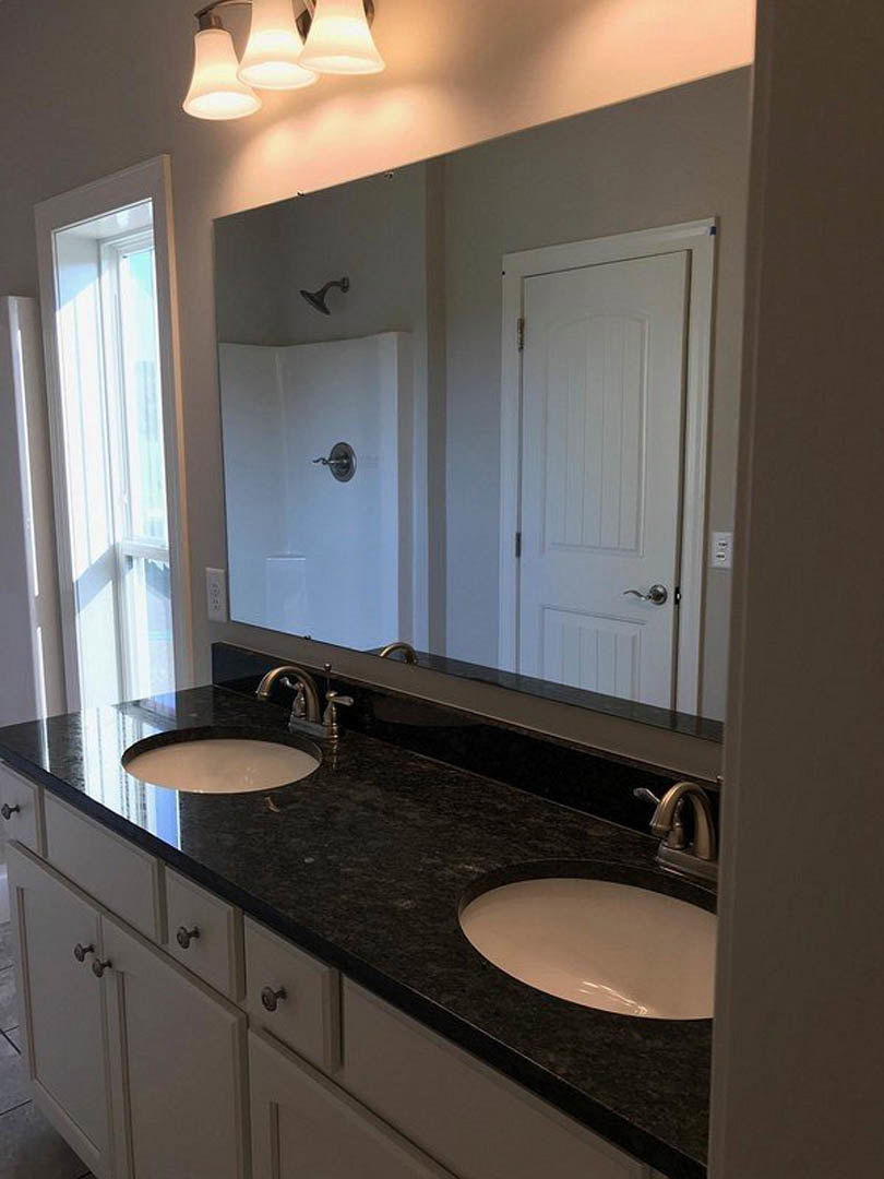 Bathroom with double vanity featuring undermount sinks, expansive wall mirror, quartz countertop, modern faucets, white cabinetry, and tiled walls