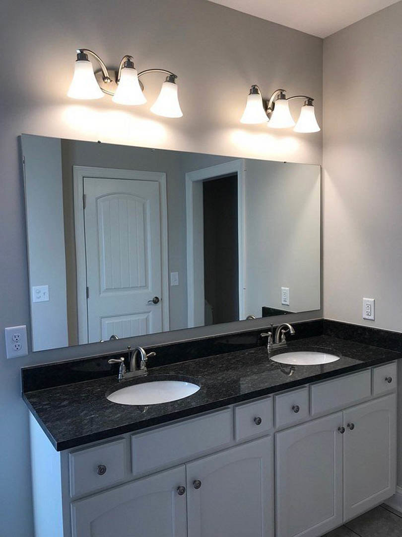 Bathroom featuring a wide mirror above a black countertop sink, white cabinetry with black handles, three-light fixture, tiled walls, and visible electrical outlet.