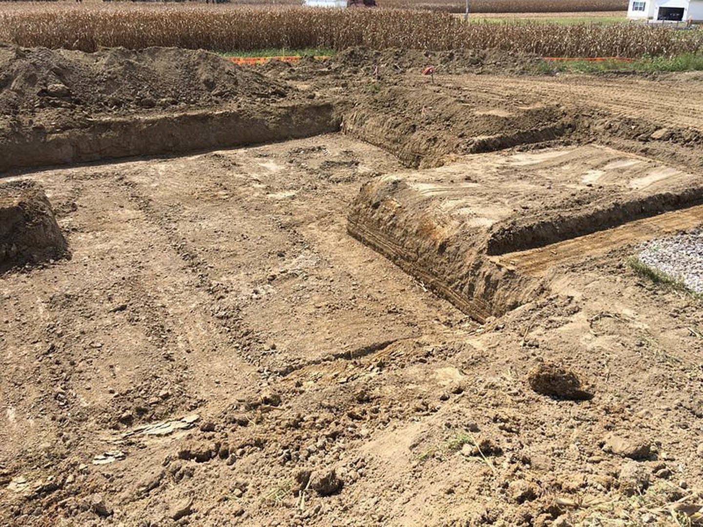 Brown dirt field with patches of grass and soil, blurred building in the background