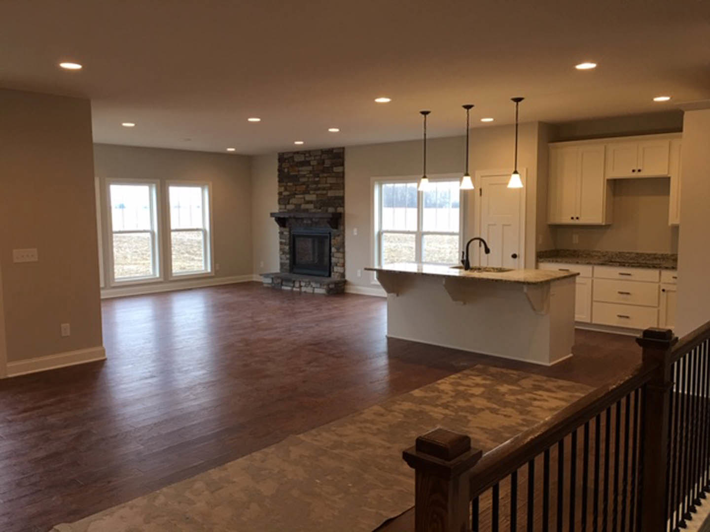Open concept living room with stone fireplace, brown carpet over hardwood floor, adjacent kitchen featuring tile backsplash, cabinetry, and laminate countertop with sink, large