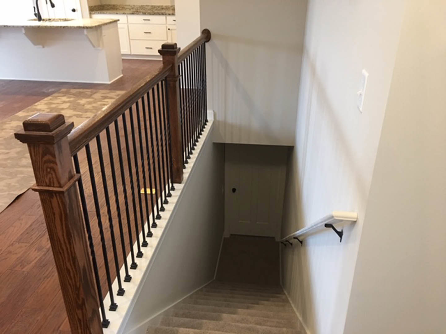 Wood staircase with black metal balusters, wooden handrail, white walls, and a white door at the landing.