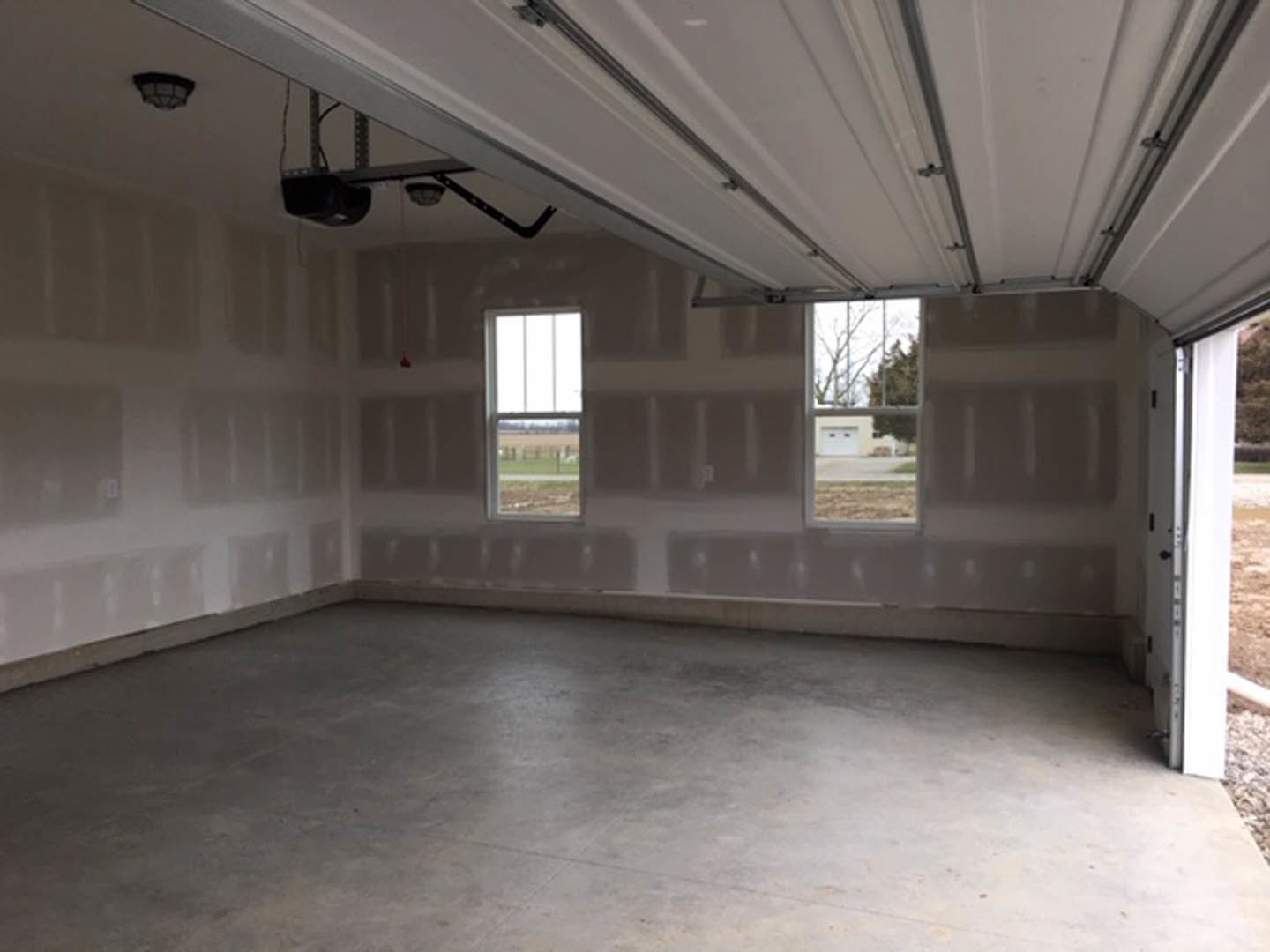 Open-concept room featuring a glass-panel garage door, multiple windows with field views, grey flooring, white plaster walls, and a black glass light fixture.