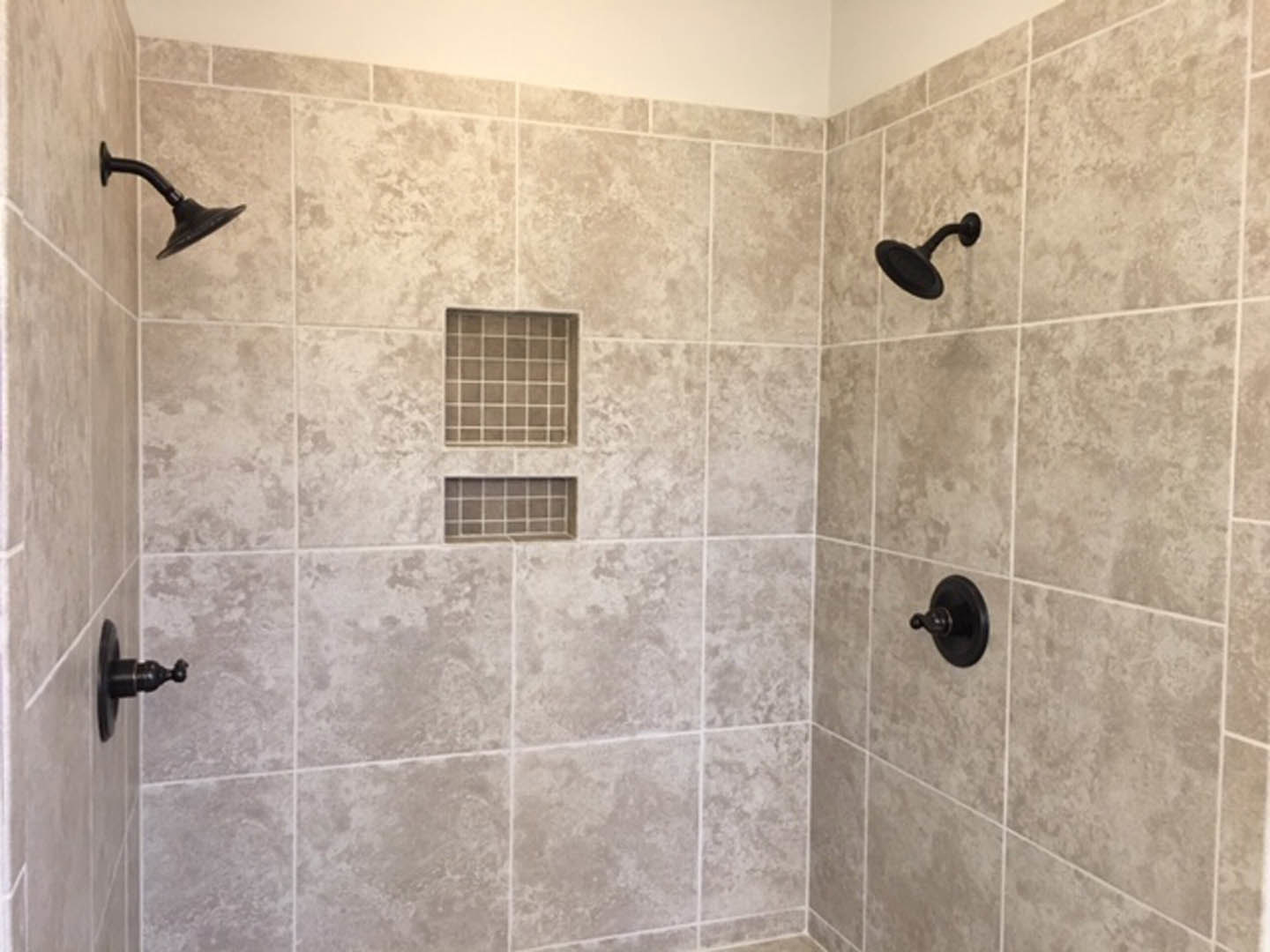 Modern bathroom shower featuring a tiled wall with large rectangular tiles, chrome shower head, and glass enclosure.