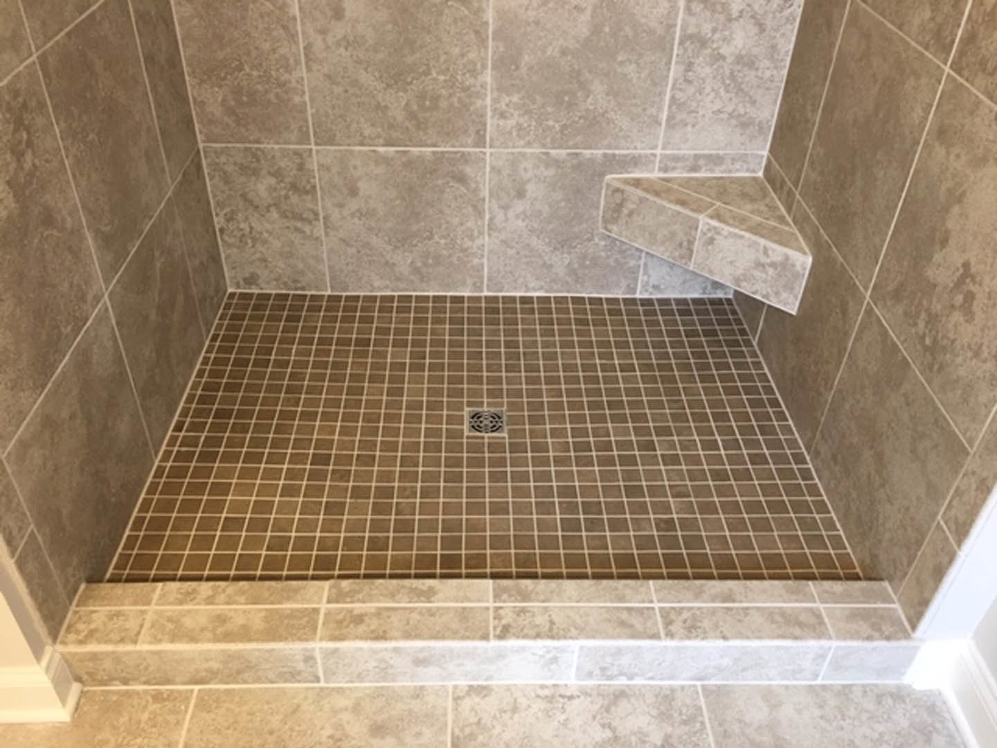 Walk-in shower with marble tile walls, granite accent trim, chrome shower head, and tiled floor with central drain