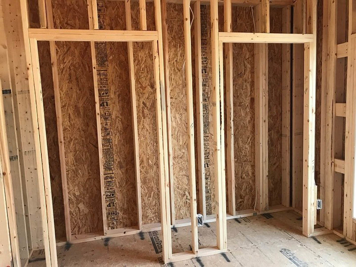 Wood-framed window with exposed beams and insulation, tape measure resting on sill in unfinished interior room
