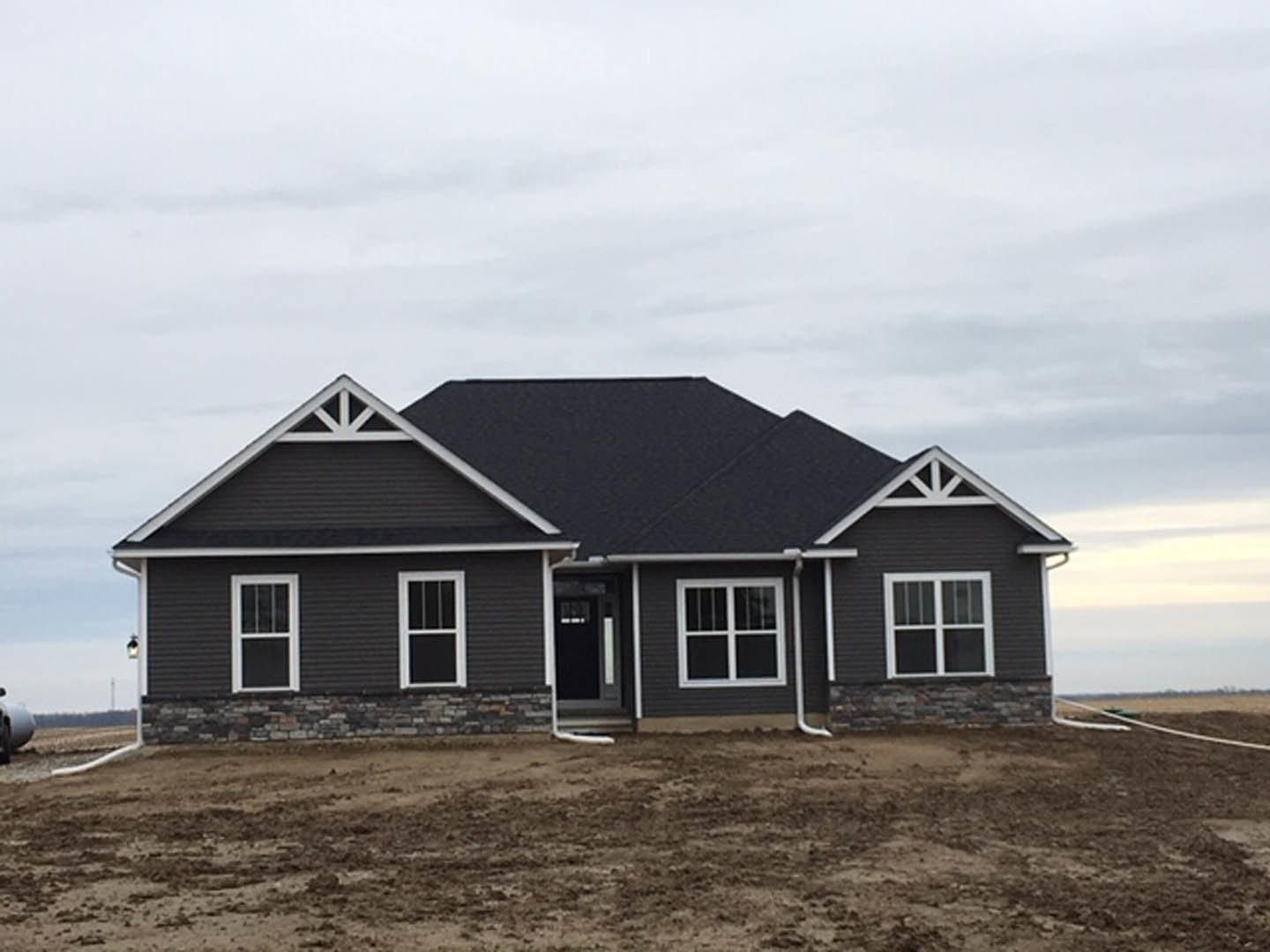 Modern house with black roof, white-framed windows, and dirt field in foreground featuring a white pipe