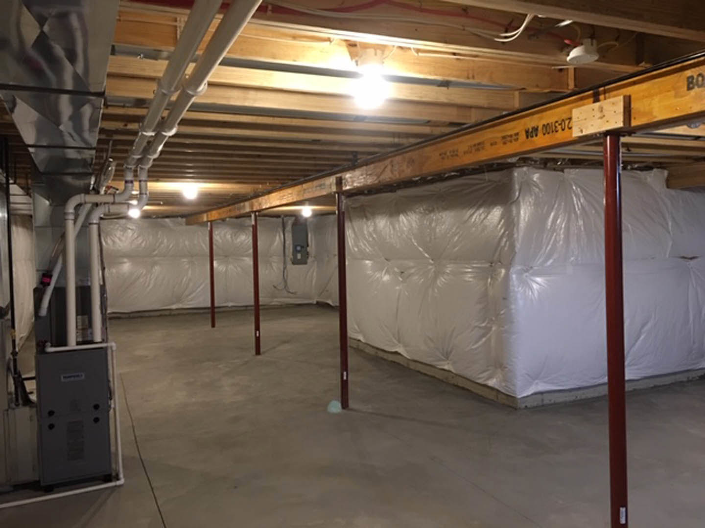Unfinished basement with exposed steel beams, concrete floor, white walls, and a large white bag placed against one wall