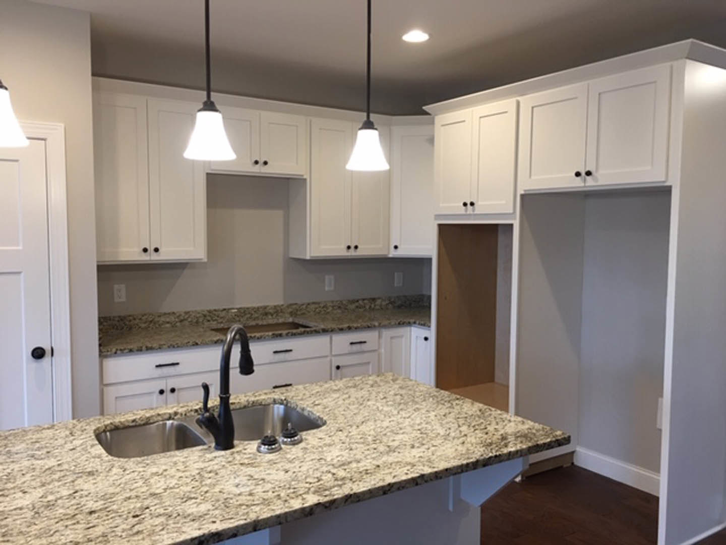 White kitchen with granite countertops, stainless steel sink and faucet, tile backsplash, white cabinetry, and modern light fixture.