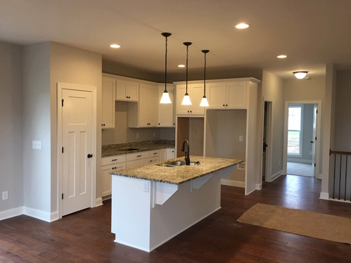 Modern kitchen with tile flooring, central island featuring built-in sink, white cabinetry, stone countertops, pendant lights hanging from ceiling, and neutral wall finishes