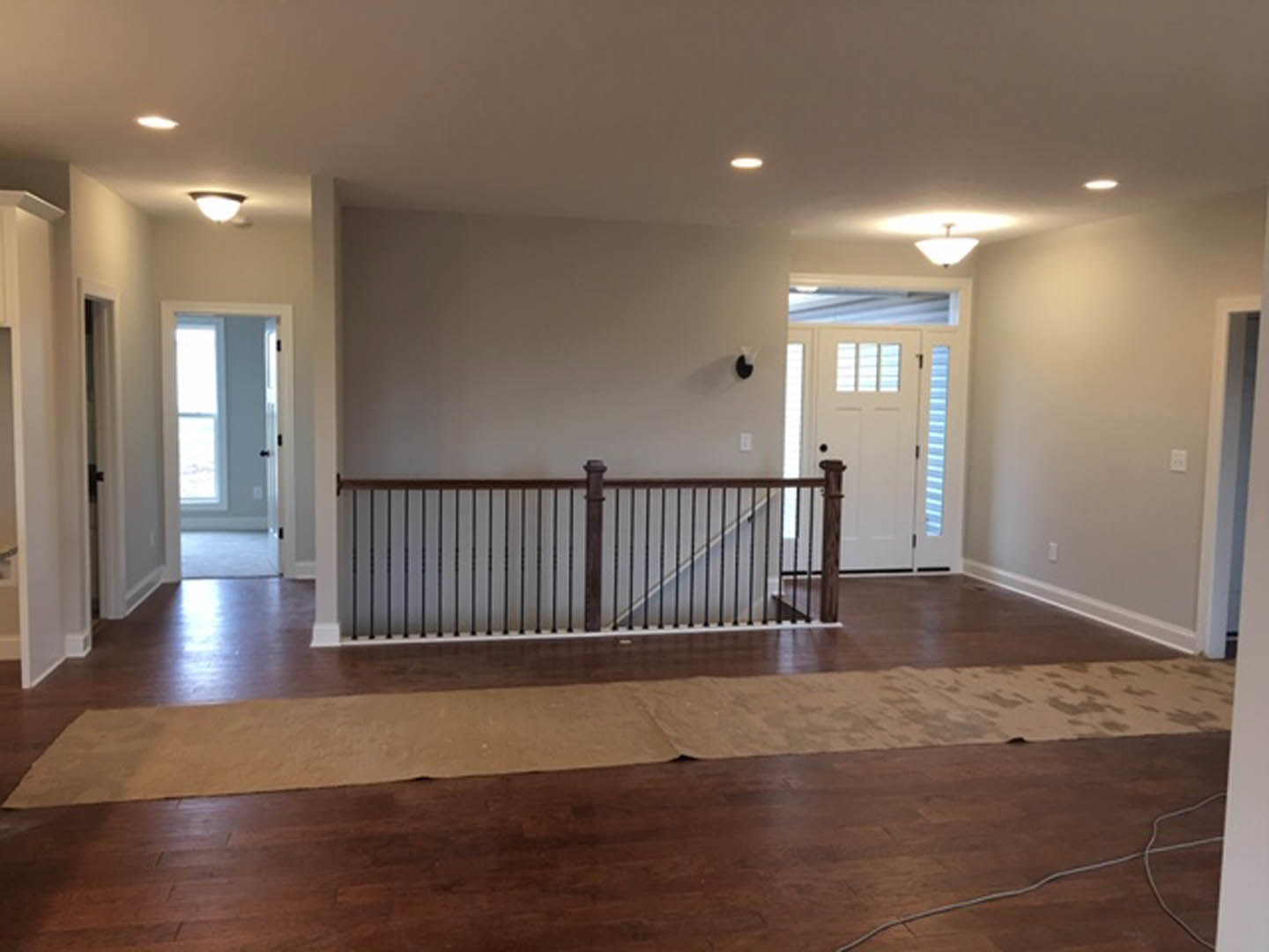 Staircase with dark wood railing, white door with glass window, brown rug on hardwood floor, white wire on wood surface, blue and white striped accent wall in background
