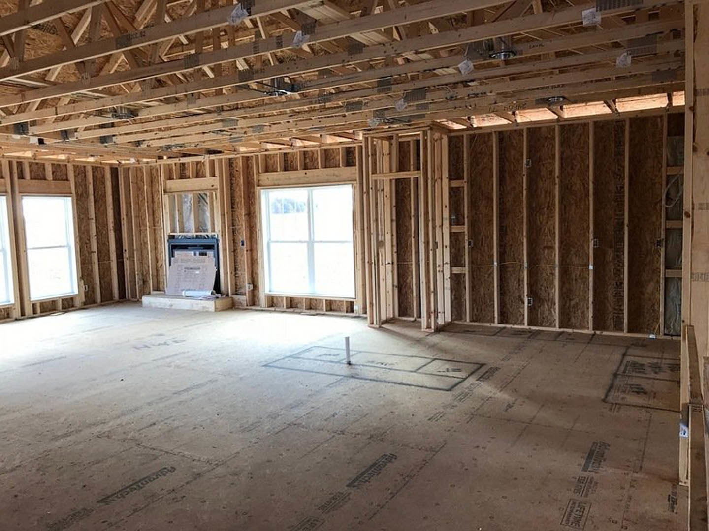 Living room with exposed wood ceiling beams, stone fireplace, white-framed window, and hardwood flooring