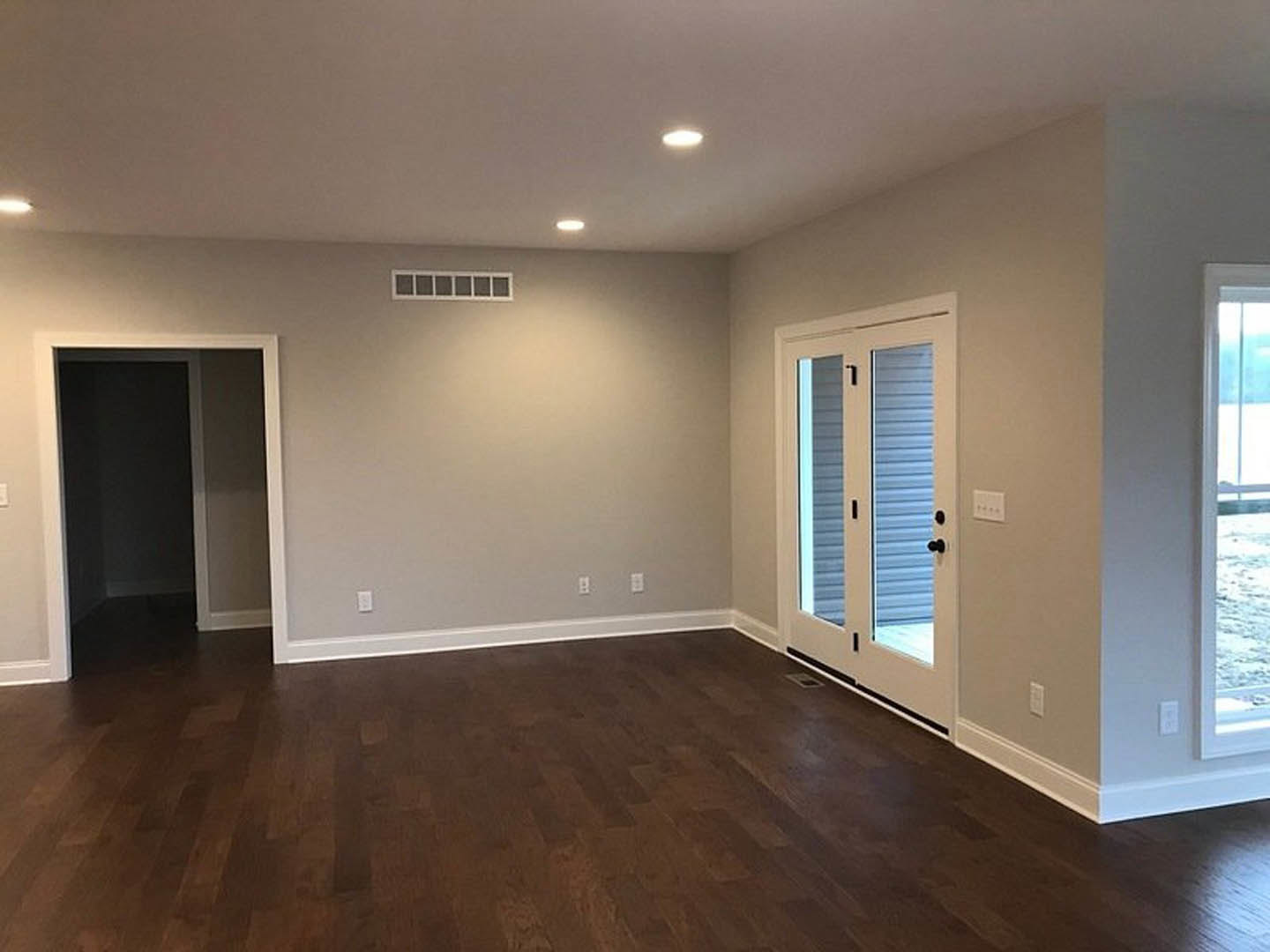 Dark wood flooring, white plaster walls, open door leading to a room with large window overlooking the ocean.