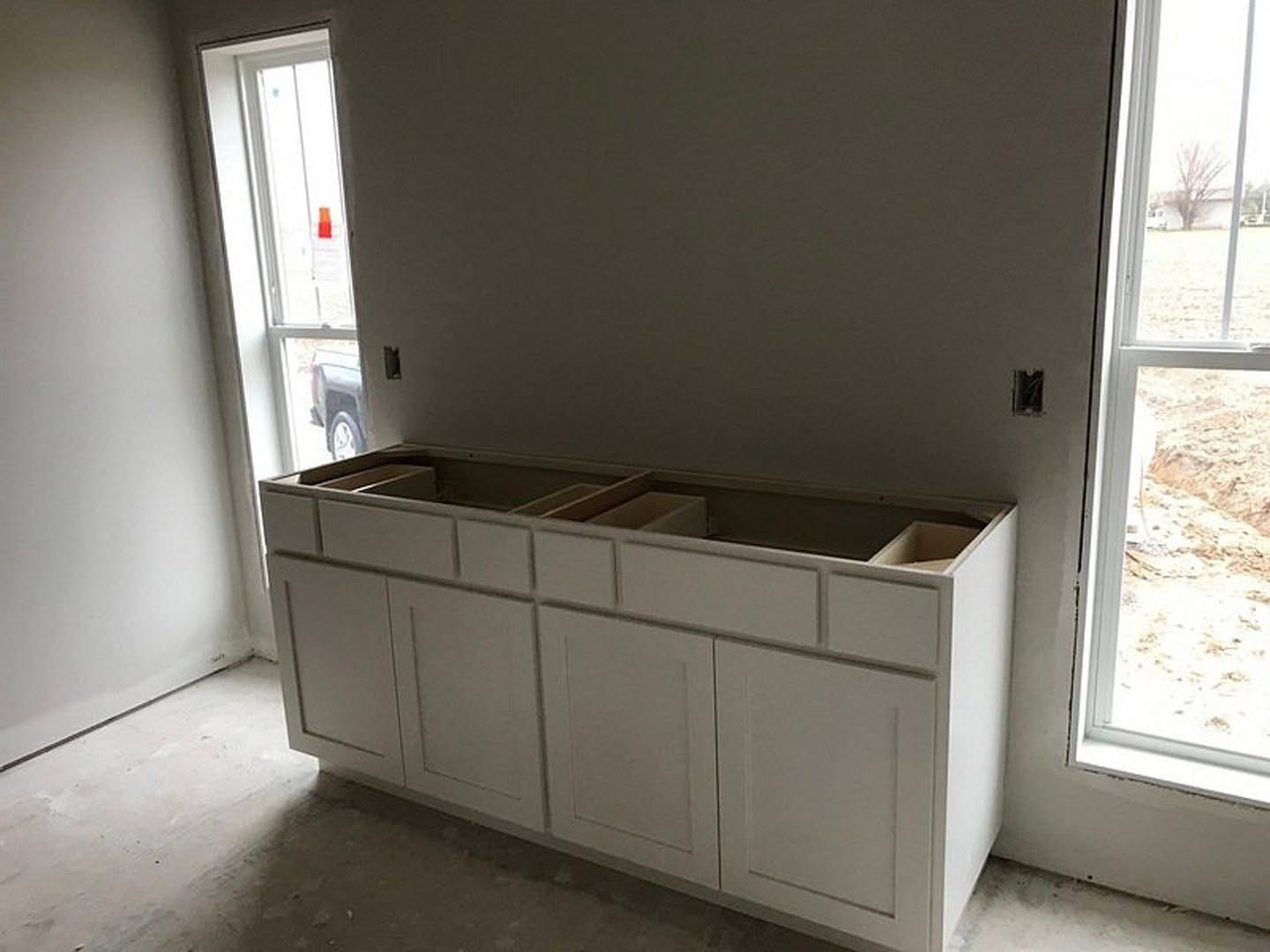 White kitchen cabinets with drawers and silver handles, light plaster walls, window above sink, wood flooring