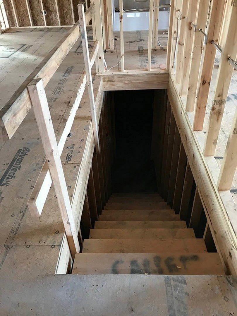 Wood plank staircase with composite handrail ascending from ground floor, surrounded by dark walls and doorway, indoor residential setting.