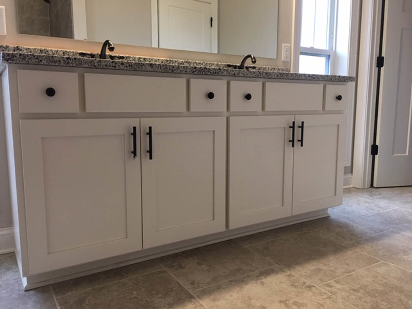 Bathroom with white shaker cabinets, black hardware, marble countertops, undermount sink, and light tile flooring