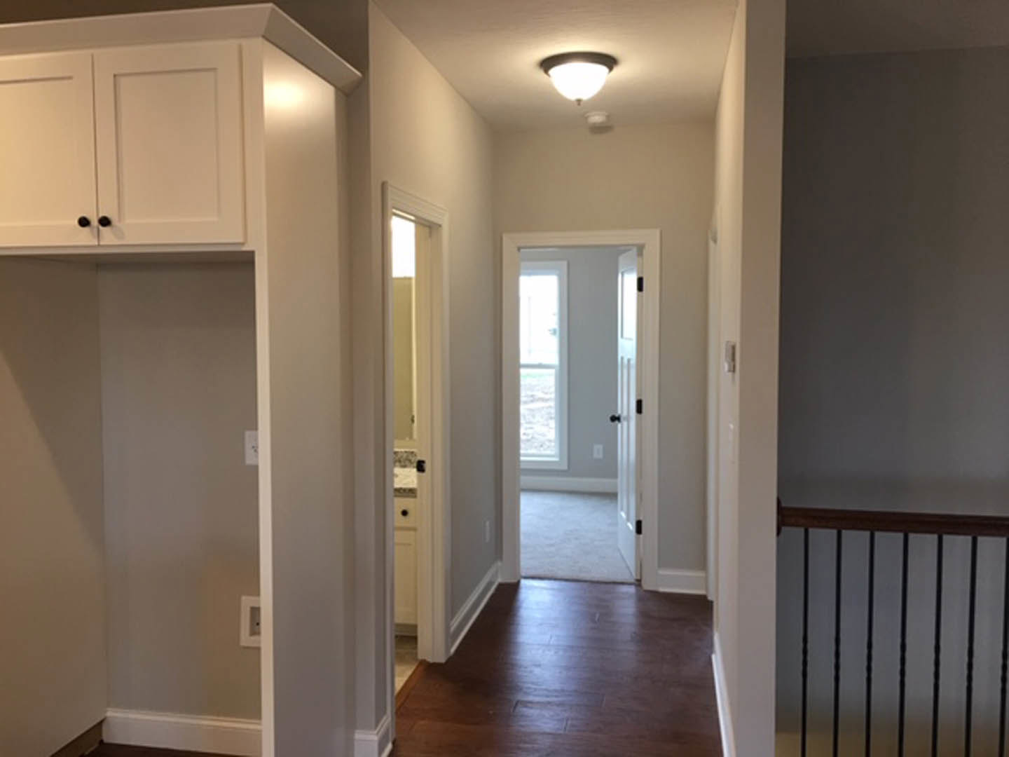 Hallway with white walls, dark hardwood floor, white trim, white door with window, close-up of railing, ceiling light fixture