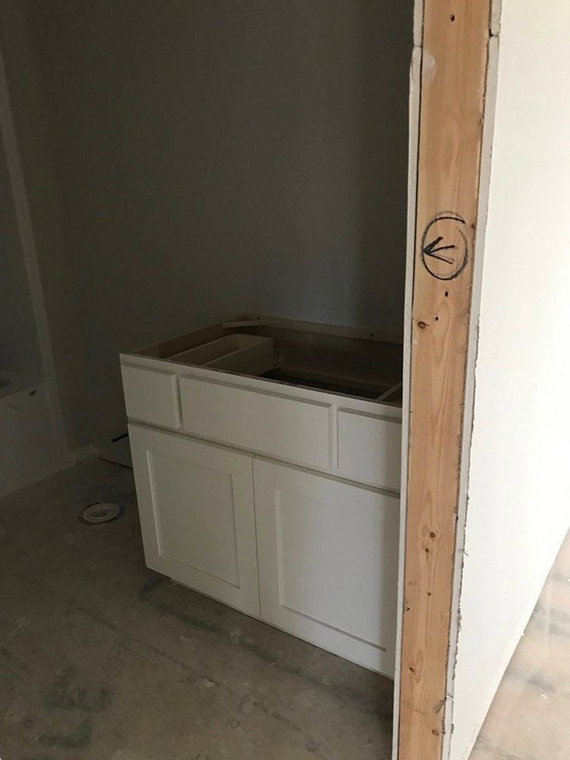 White shaker-style kitchen cabinets and drawers with brushed metal handles, light wood flooring, and smooth plaster walls.