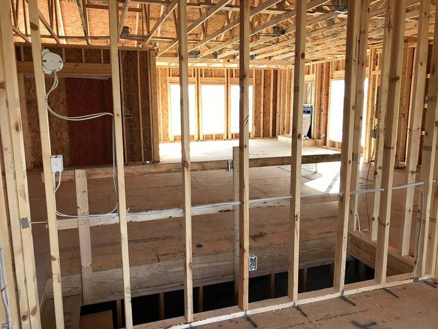 Wood framing and exposed beams in a room under construction, window opening visible, white rectangular object with black circle leaning against unfinished wall