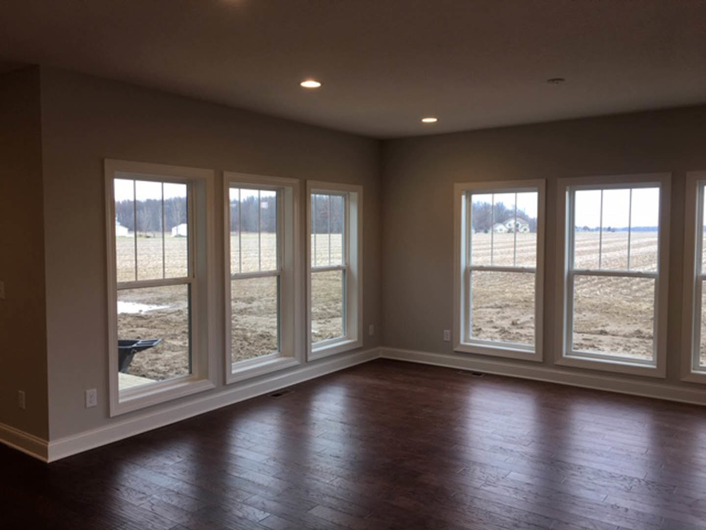 Spacious room with dark wood flooring, multiple large windows, and views of an open field