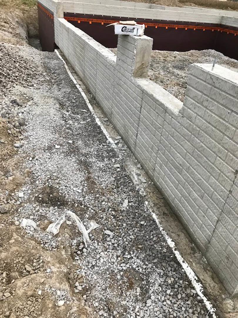 White stucco wall with concrete pillar base, adjacent to red brick wall and dirt driveway, exterior residential facade
