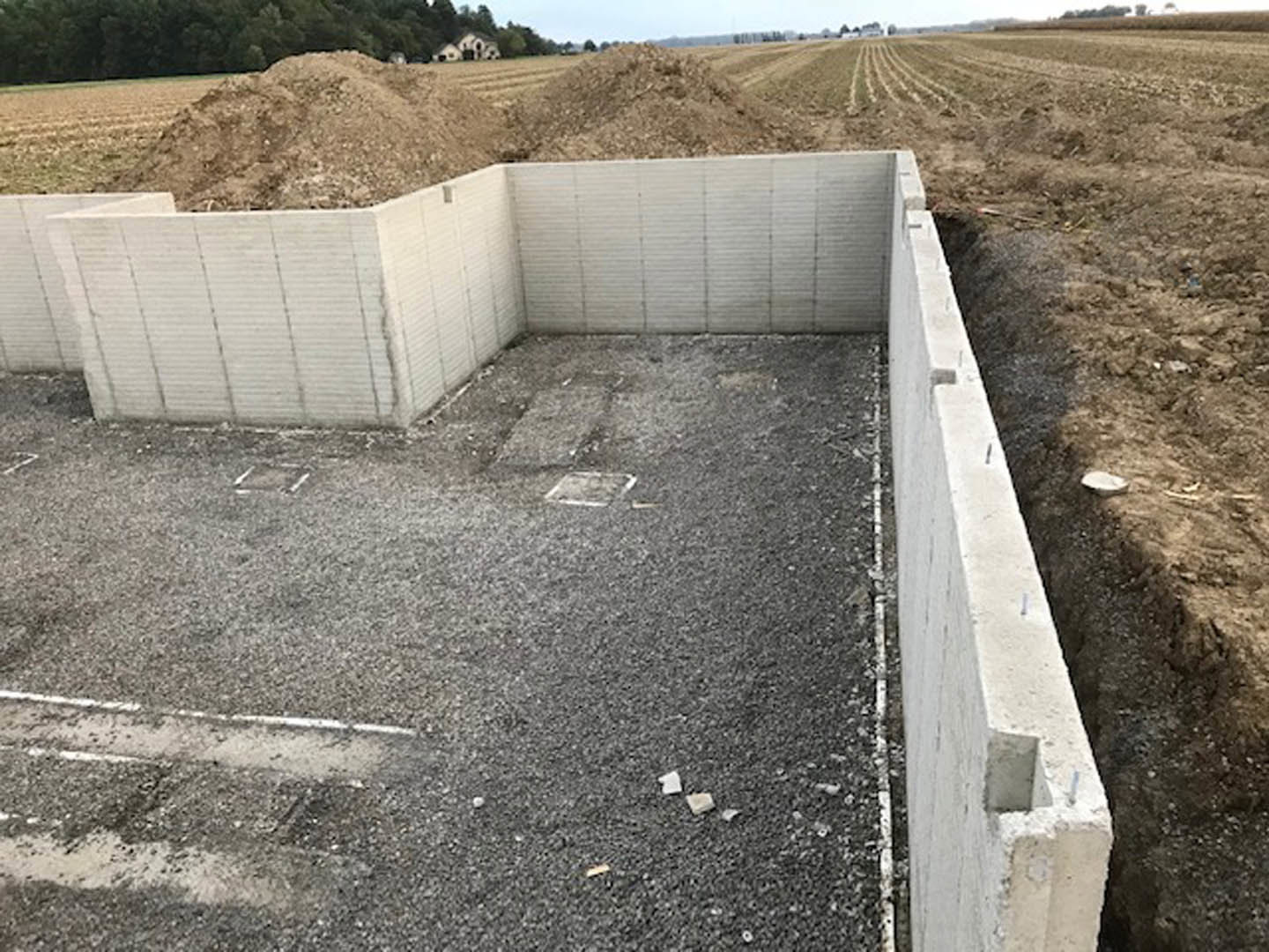 Concrete foundation surrounded by exposed soil and dirt, outdoor construction site with sky and sparse plants in the background