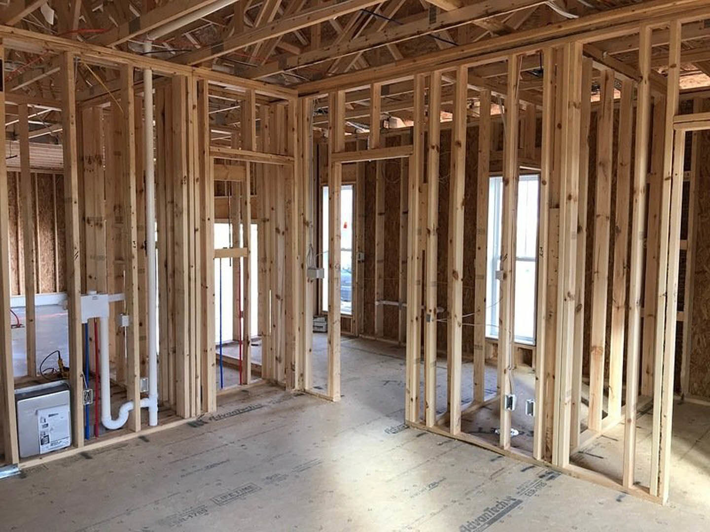 Unfinished room with exposed wood framing, ceiling beams, and a large window letting in natural light
