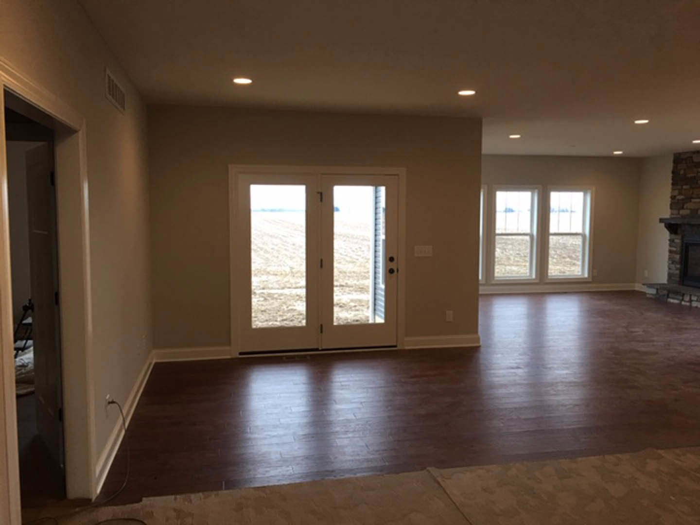 Bright room with double glass-paneled doors, large windows overlooking a field, wood flooring, neutral walls, and a patterned rug.
