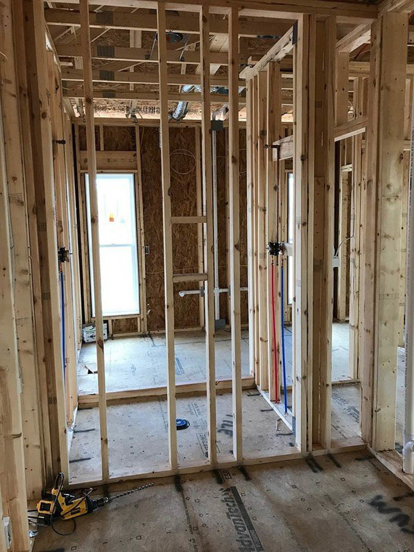 Unfinished room with exposed wood framing, window letting in natural light, yellow and black drill on subfloor, construction sign visible
