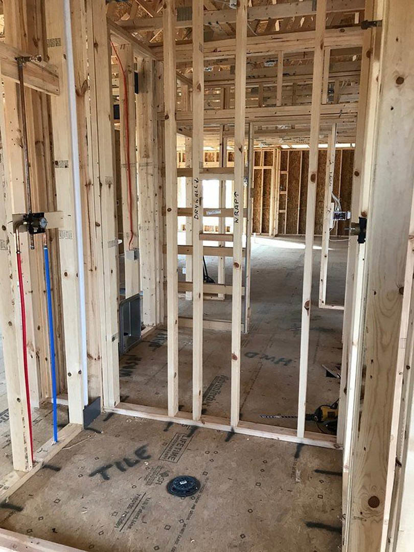 Exposed wood framing and beams in a house under construction, with visible insulation, a ladder, and unfinished walls.