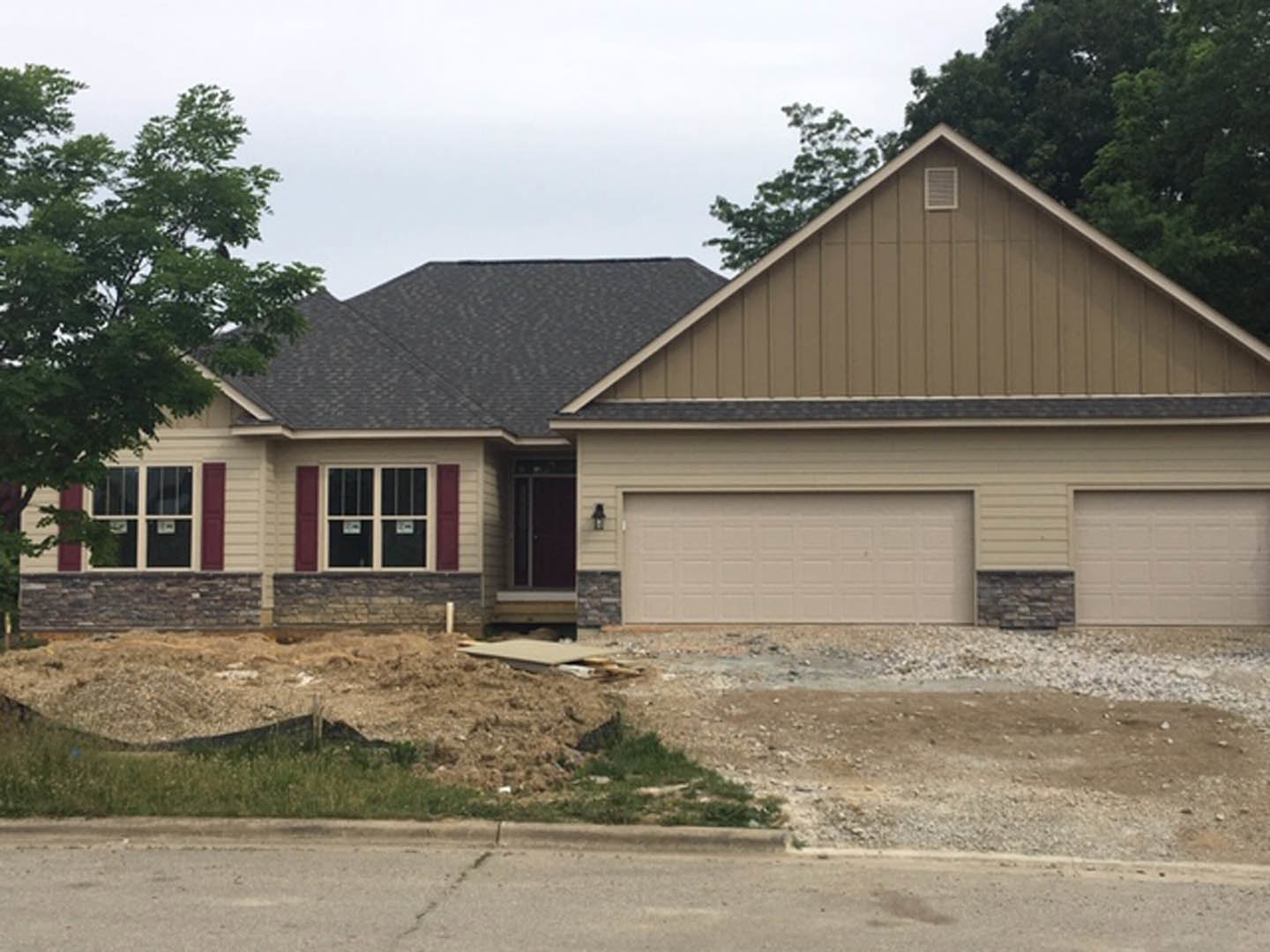 Two-story home with white siding, prominent white garage door, paved driveway, mature trees surrounding the property, and windows framed by metal accents