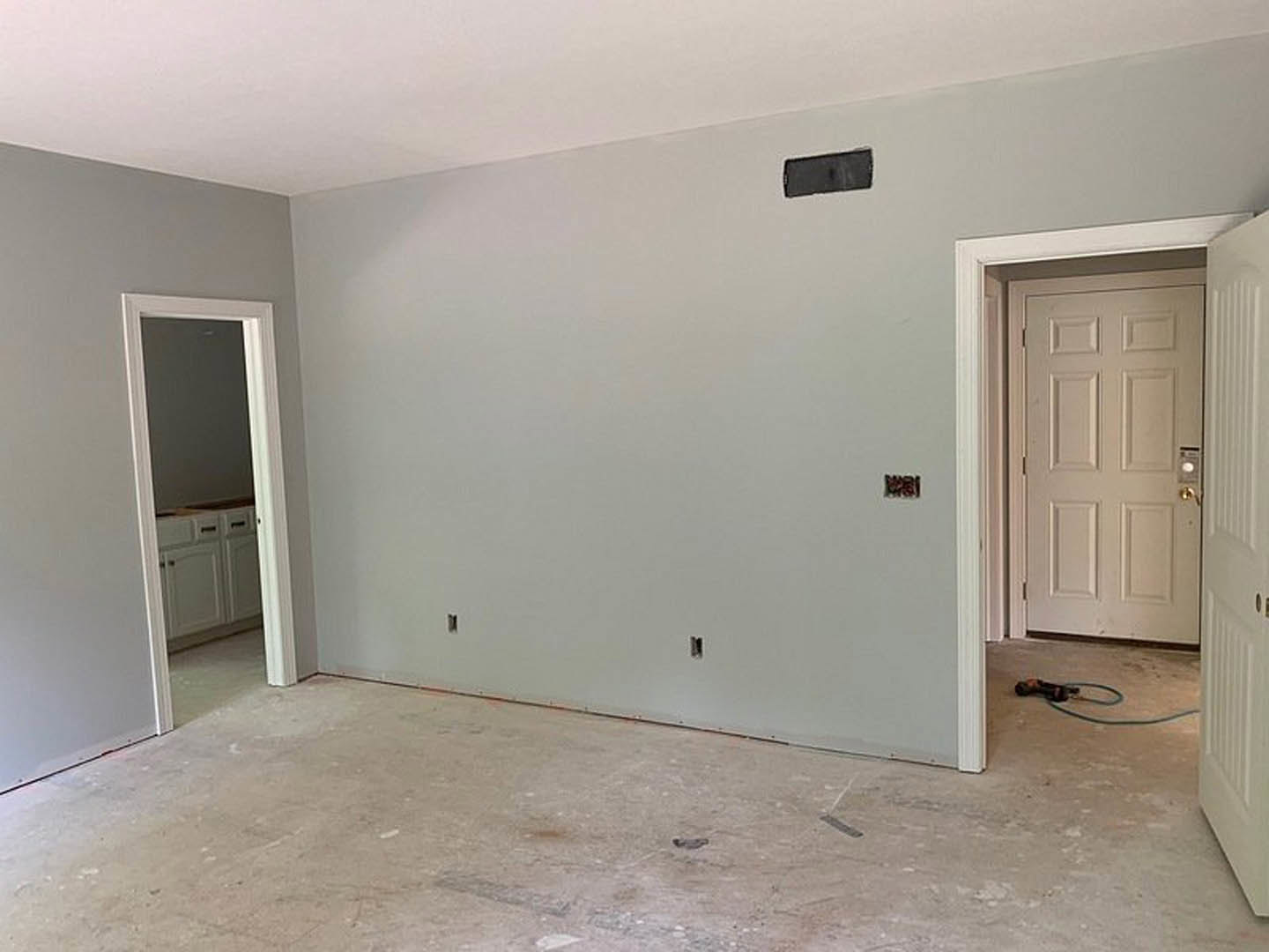 White paneled door with silver handle set in a smooth white wall, light wood flooring, black cord resting on floor near door.