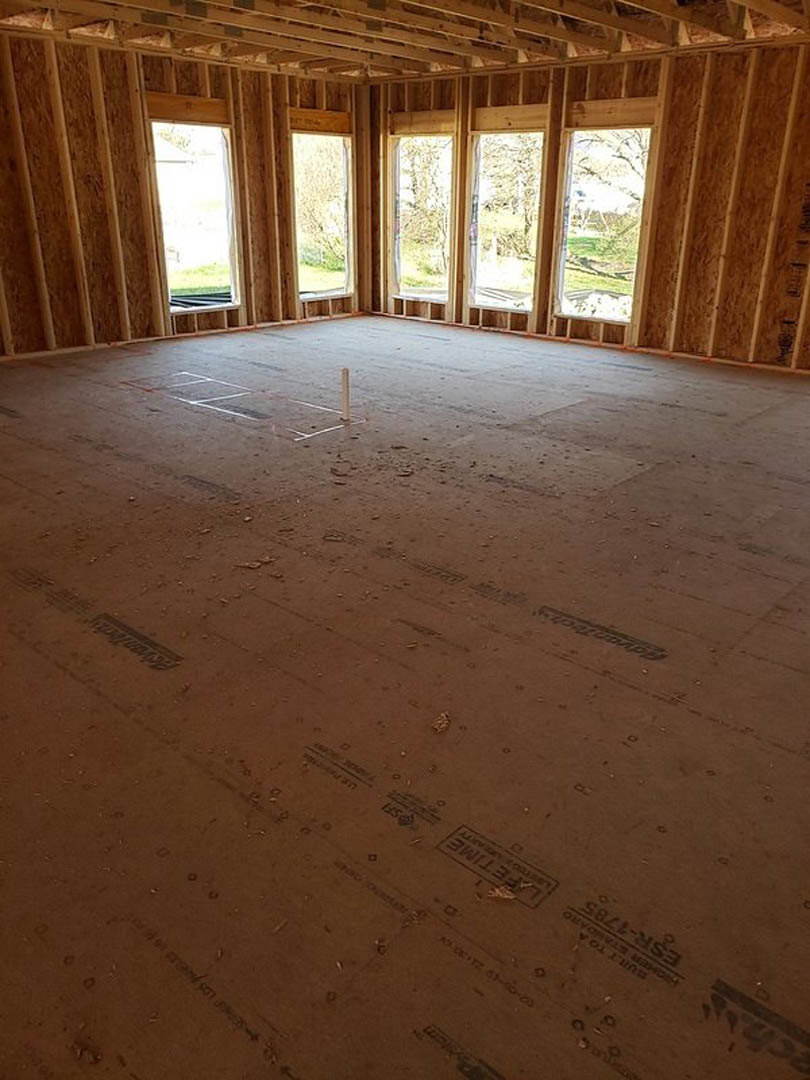 Concrete floor room with several windows, white support pole, exposed wood beam ceiling, natural daylight streaming through glass panes