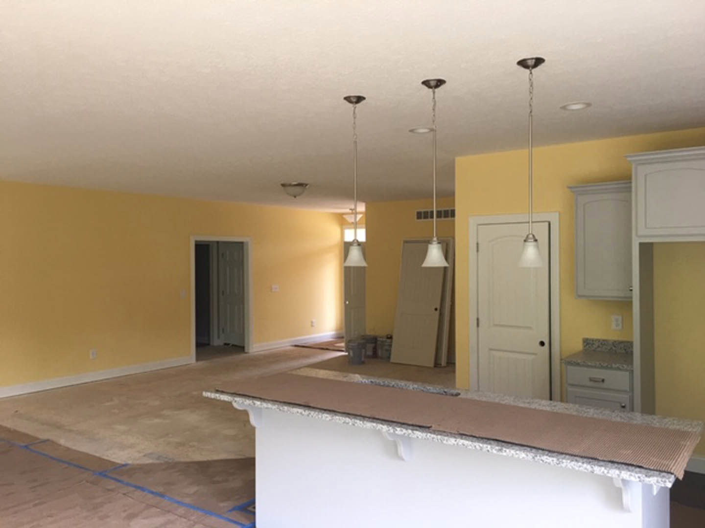 Kitchen and dining room with yellow walls, white countertop, tile flooring, white door with black knob, ceiling lamp, plaster finishes